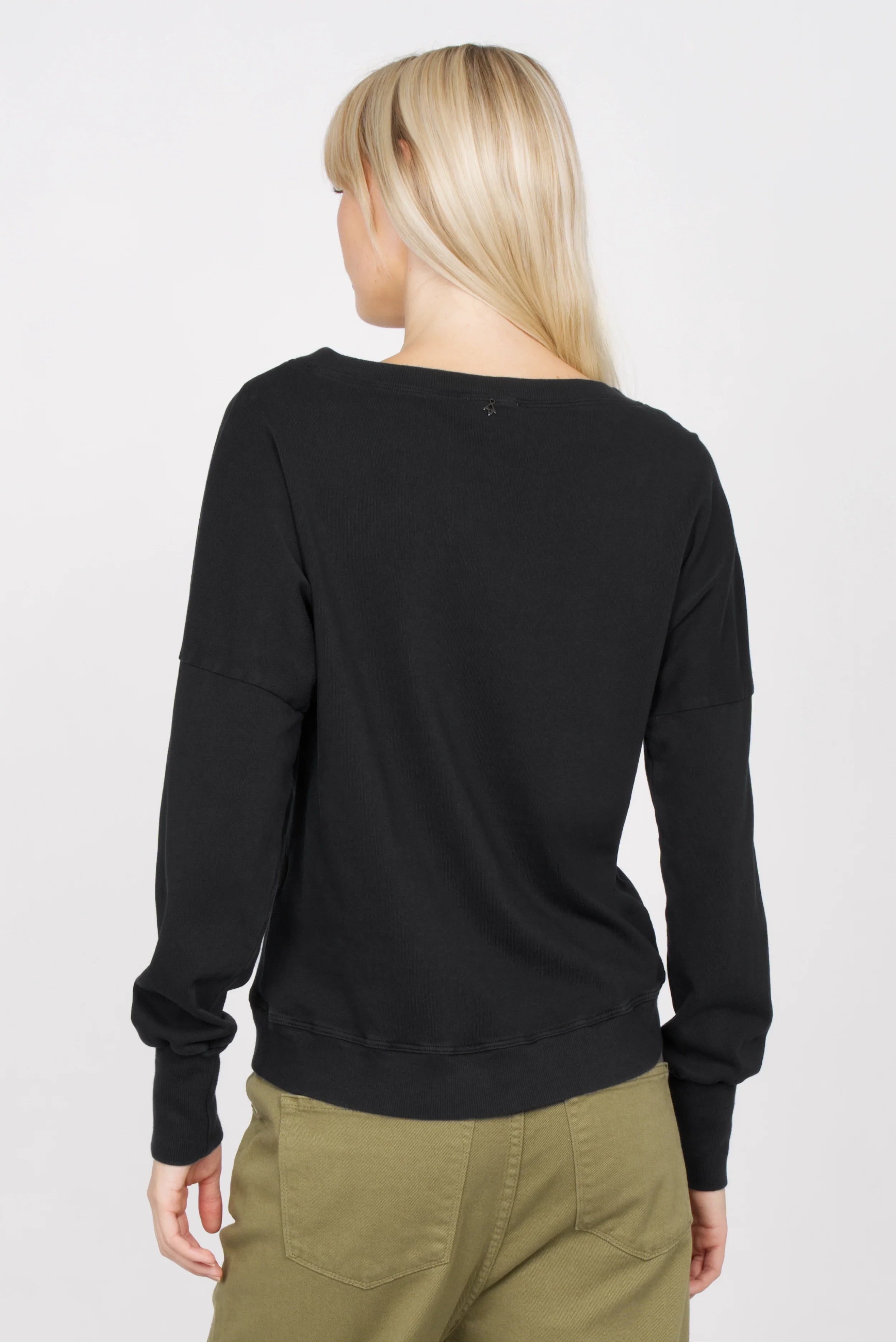 Damen trägt schwarzes RIISA Longsleeve mit überschnittenen Schultern und extrabreiten Rippbündchen von hinten gesehen