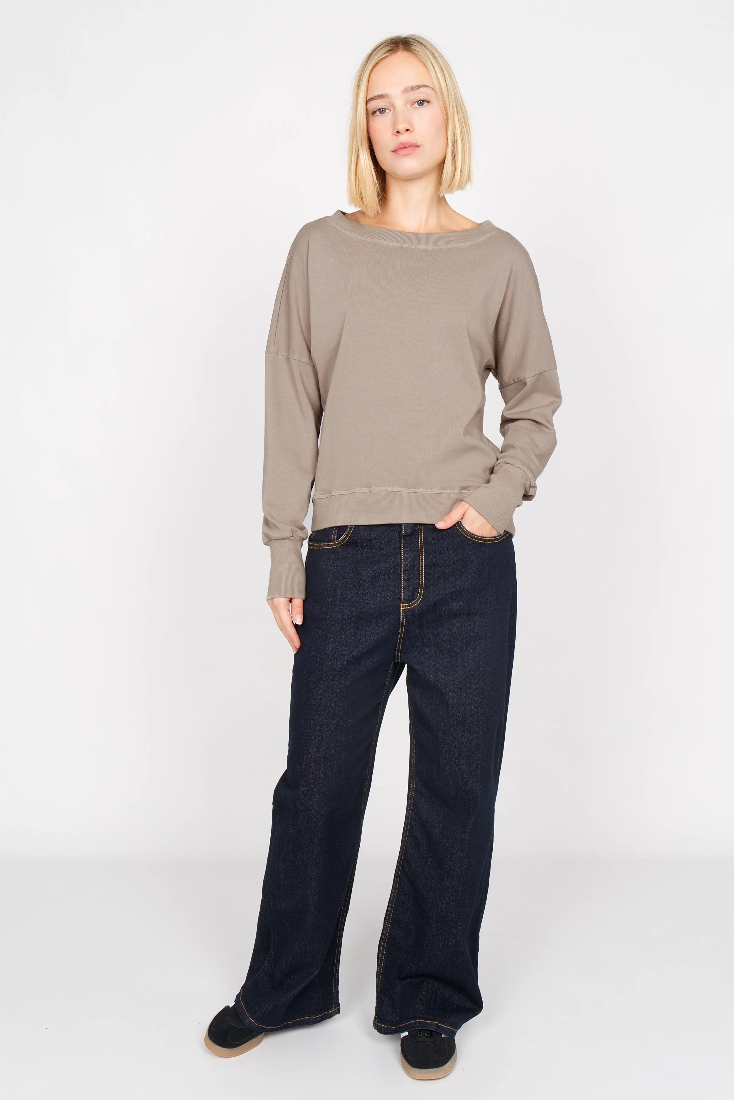 Frau trägt taupefarbenes RIISA Longsleeve mit überschnittenen Schultern und extrabreiten Rippbündchen, kombiniert mit dunkelblauer Jeans
