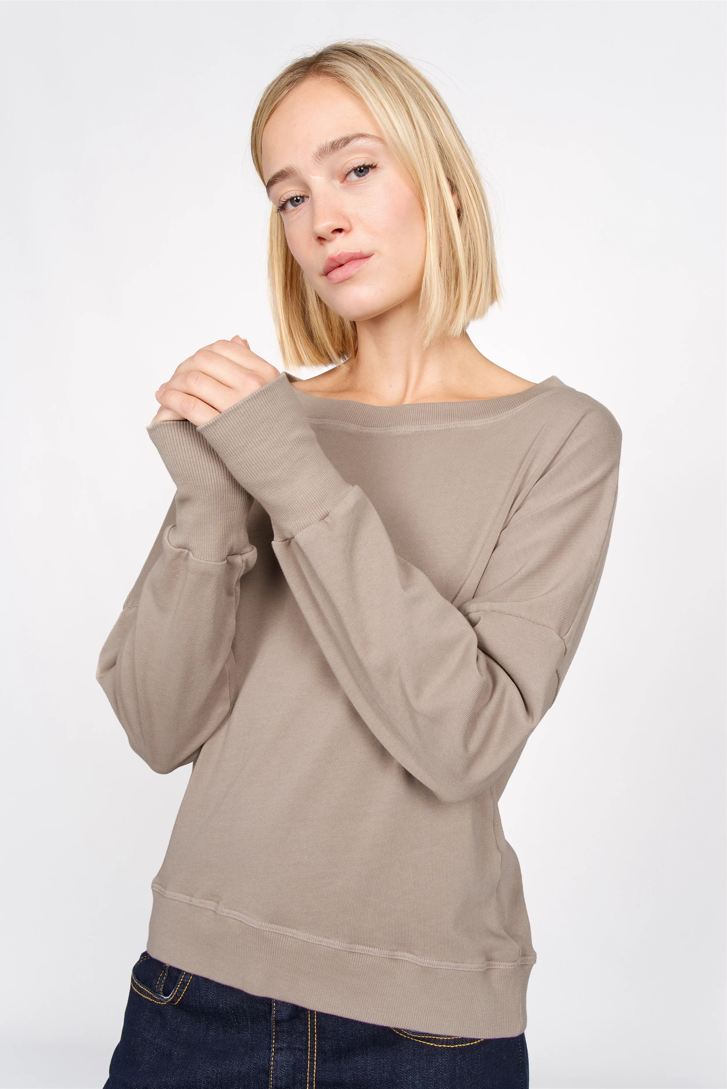 Frau trägt beige RIISA Longsleeve mit U-Boot Ausschnitt, überschnittenen Schultern und extrabreiten Rippbündchen in modernem Regular Fit