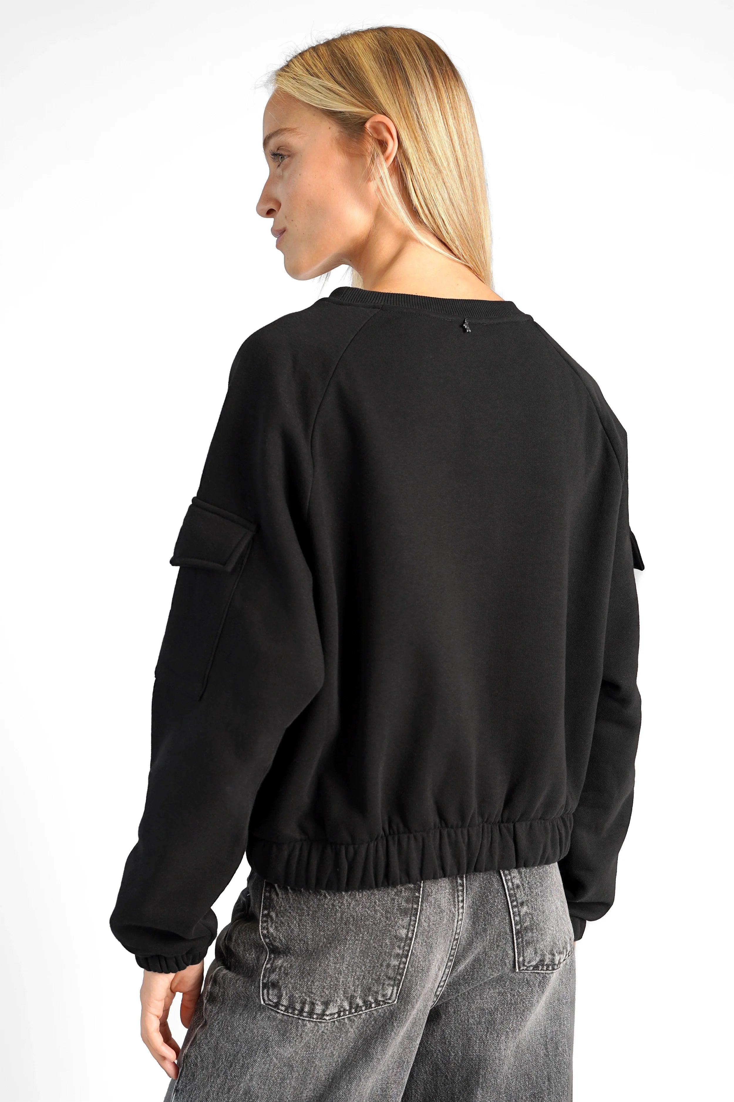 Black SEATA Cropped Sweater with oversized fit, elastic cuffs, and patch pockets on sleeves, worn with gray jeans.