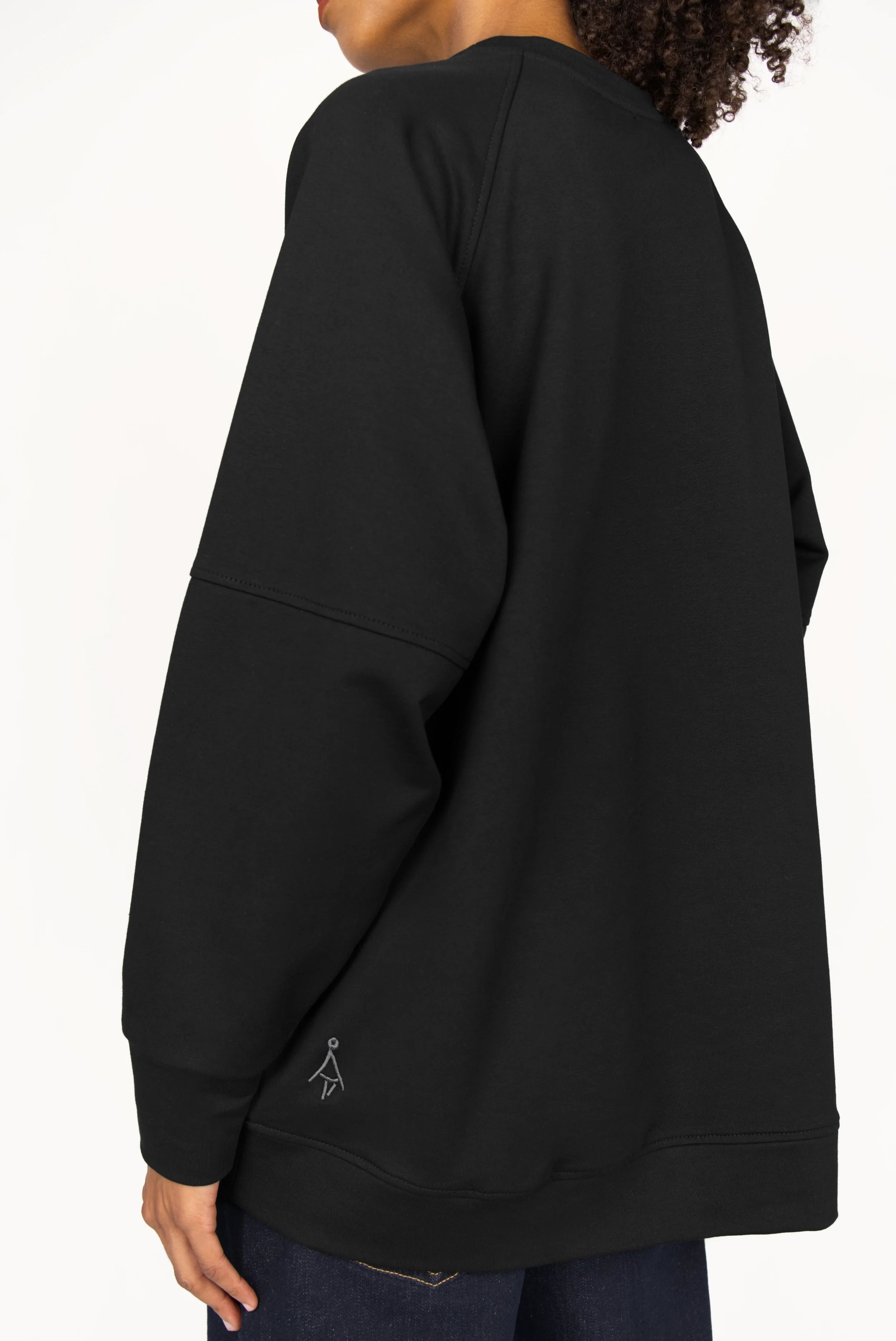 Back view of black SELKA Sweater with raglan sleeves and tonal logo embroidery, featuring wide cuffs and a slightly longer hem for relaxed, oversized fit.