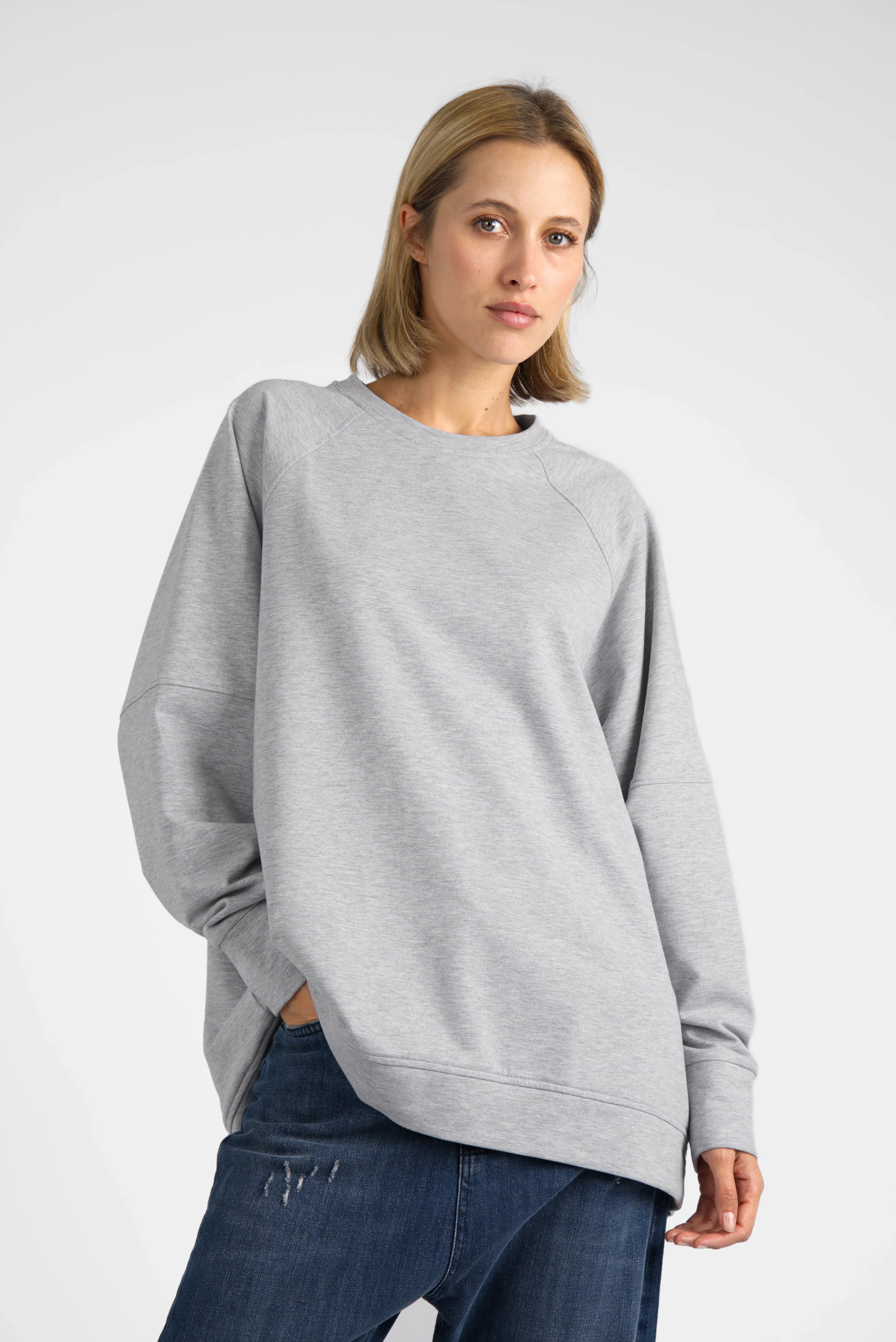 Woman wearing grey oversized SELKA Sweater with raglan sleeves and rounded hem, styled casually with jeans