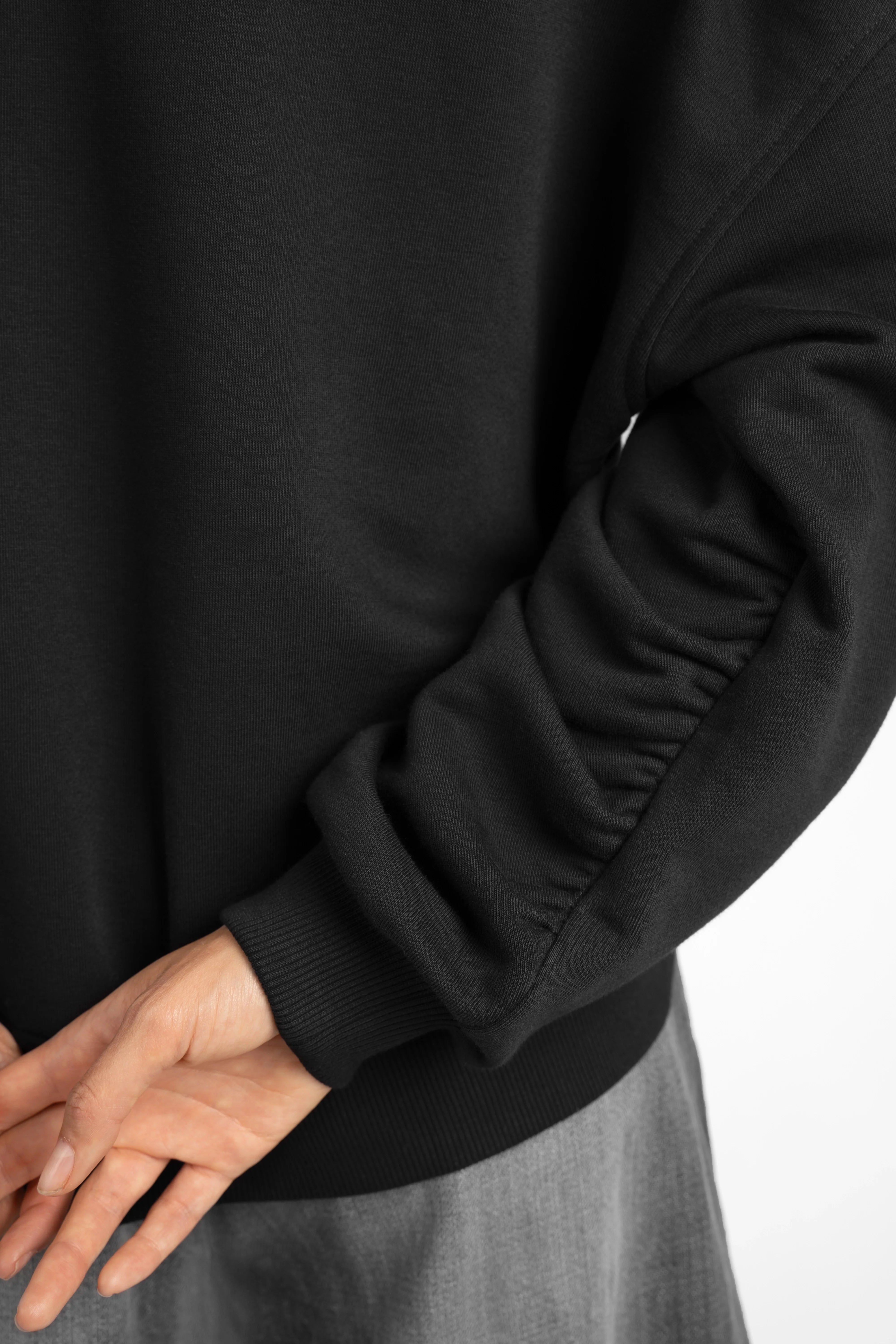 Close-up of black SEREA Sweater mit V-Ausschnitt showing ruched sleeve detail and ribbed cuff.
