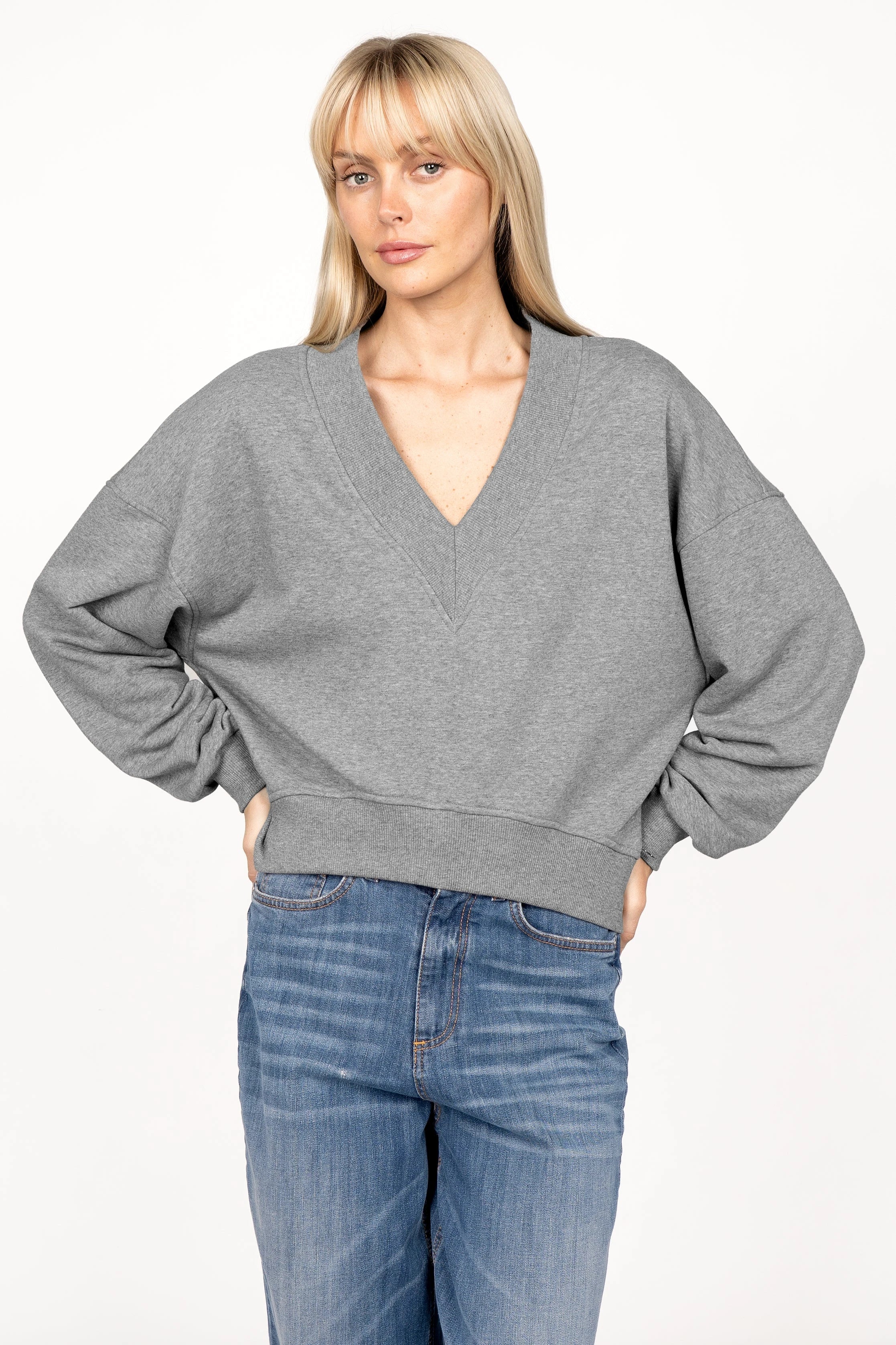 Woman wearing gray SEREA Sweater with deep V-neck and relaxed fit paired with blue jeans