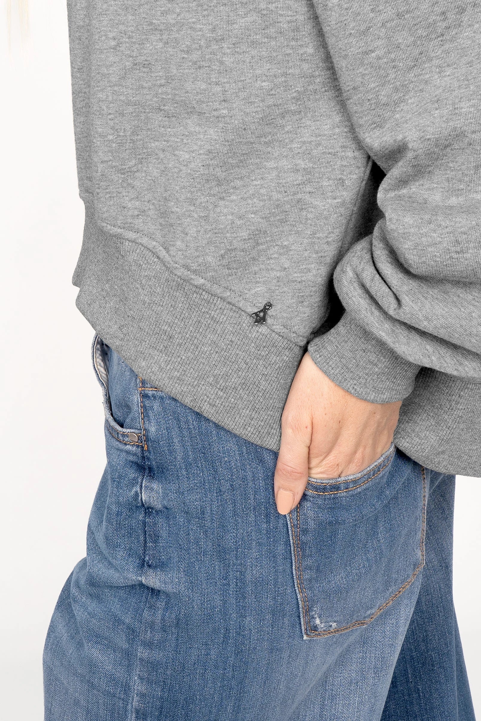 Close-up of grey SEREA Sweater with ribbed cuffs and hem, worn with blue jeans.