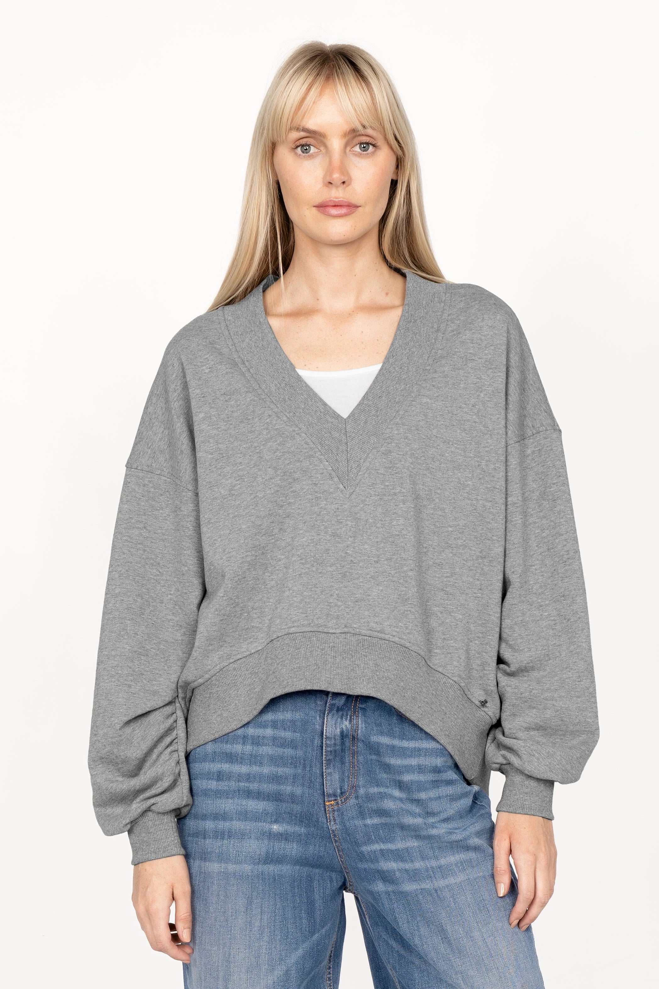 Woman wearing grey SEREA Sweater with deep V-neck, relaxed fit, and gathered sleeve detail
