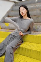 Graues SUJIN Longsleeve aus Kaschmirmix mit U-Boot-Ausschnitt und gerafften Ärmeln, slim fit, getragen von Modell auf gelben Metallstufen