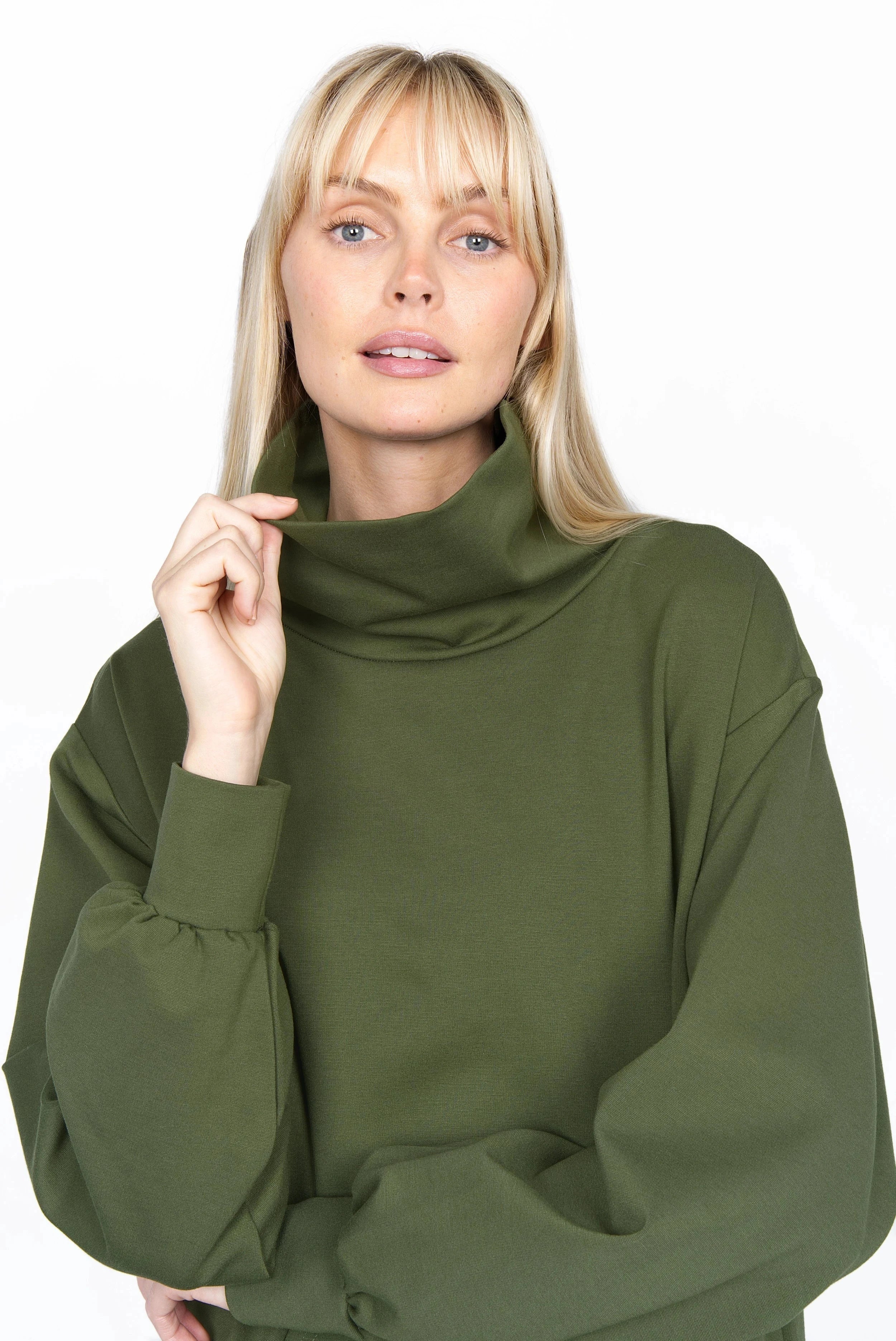 Frau trägt SYNNI Kleid aus grünem Viskose-Jersey mit Stehkragen und Kängurutasche