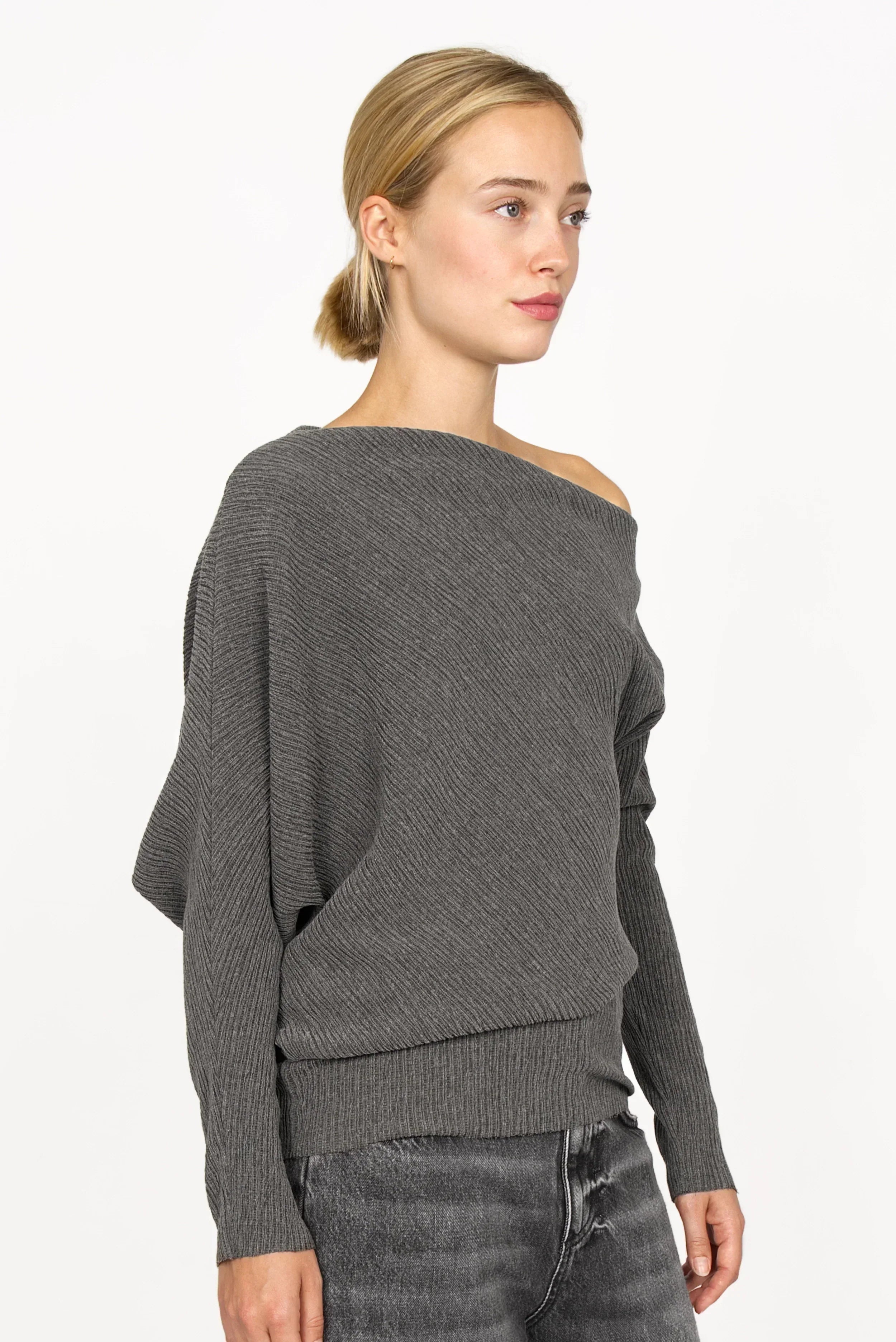 Frau trägt graues One-Shoulder Top aus plissiertem Kreppjersey mit Fledermausärmeln und asymmetrischem Schnitt