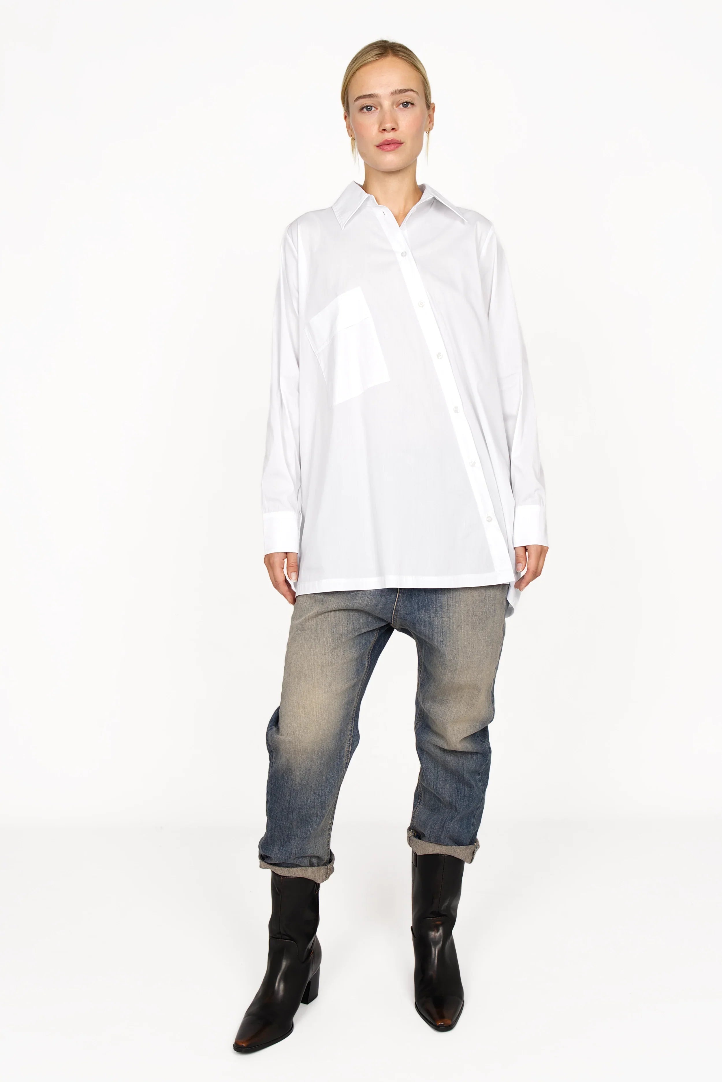 Woman wearing white oversized Hemdbluse with asymmetrical button placket, classic collar, and long sleeves paired with jeans and black boots