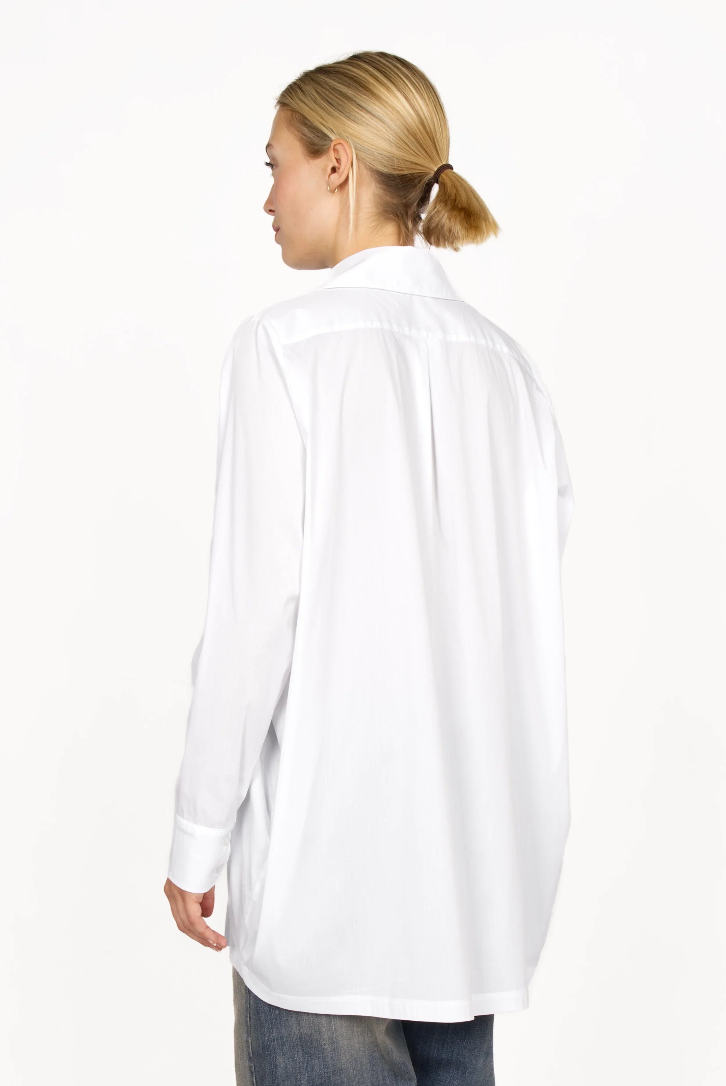 Back view of a model wearing a white oversized Hemdbluse with extended back hem and relaxed fit.