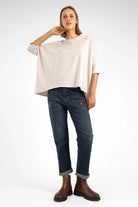 Woman wearing dark blue mid waist relaxed fit boyfriend jeans with destroyed details and rolled cuffs paired with a loose beige top and brown boots