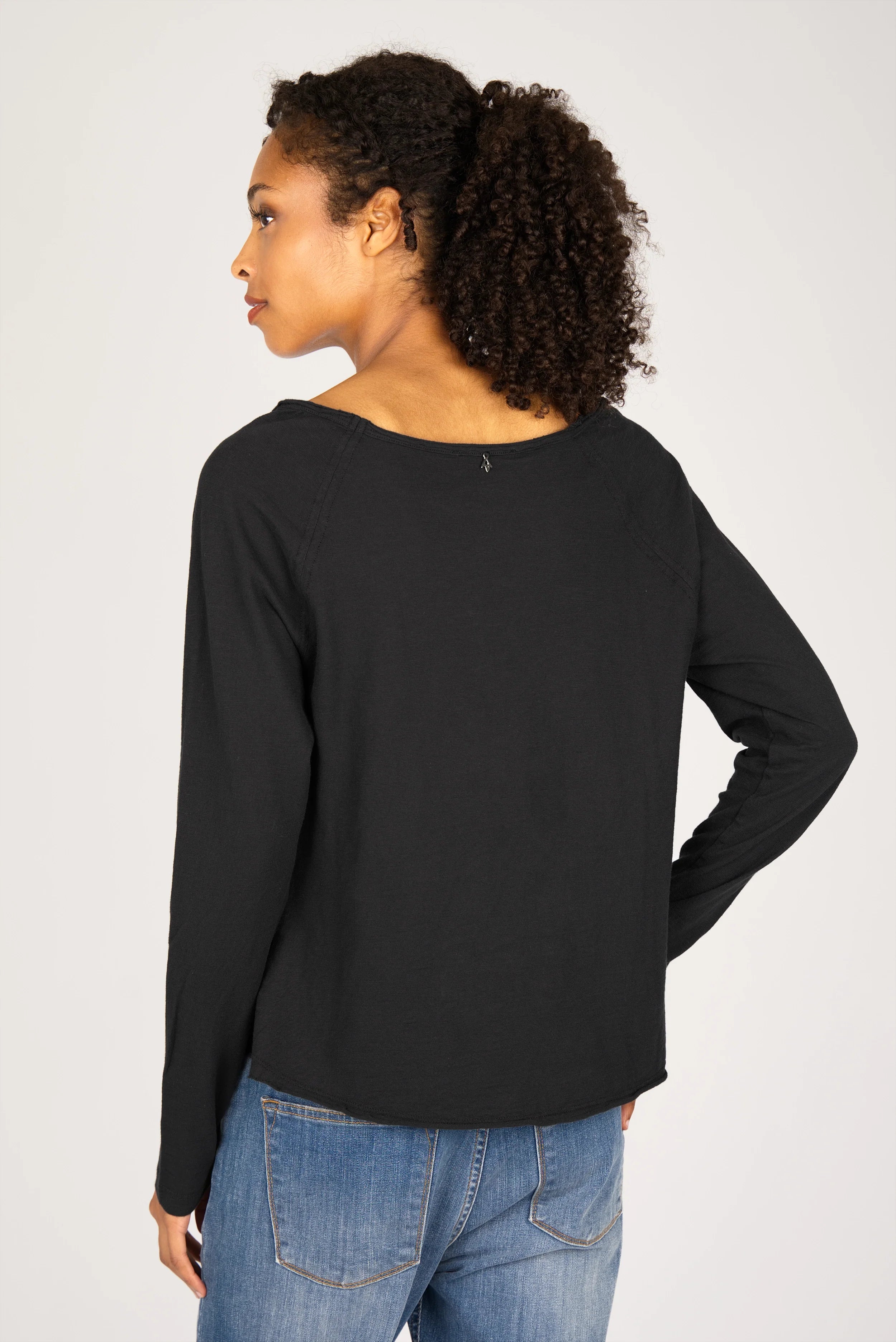 Frau trägt schwarzes TEHI Longsleeve mit Rundhalsausschnitt und extralangen Raglanärmeln von hinten gesehen