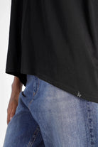 Schwarzes TIDA Blusenshirt mit V-Ausschnitt, weiter Kastenform und hinten länger geschnitten, kombiniert mit blauen Jeans.