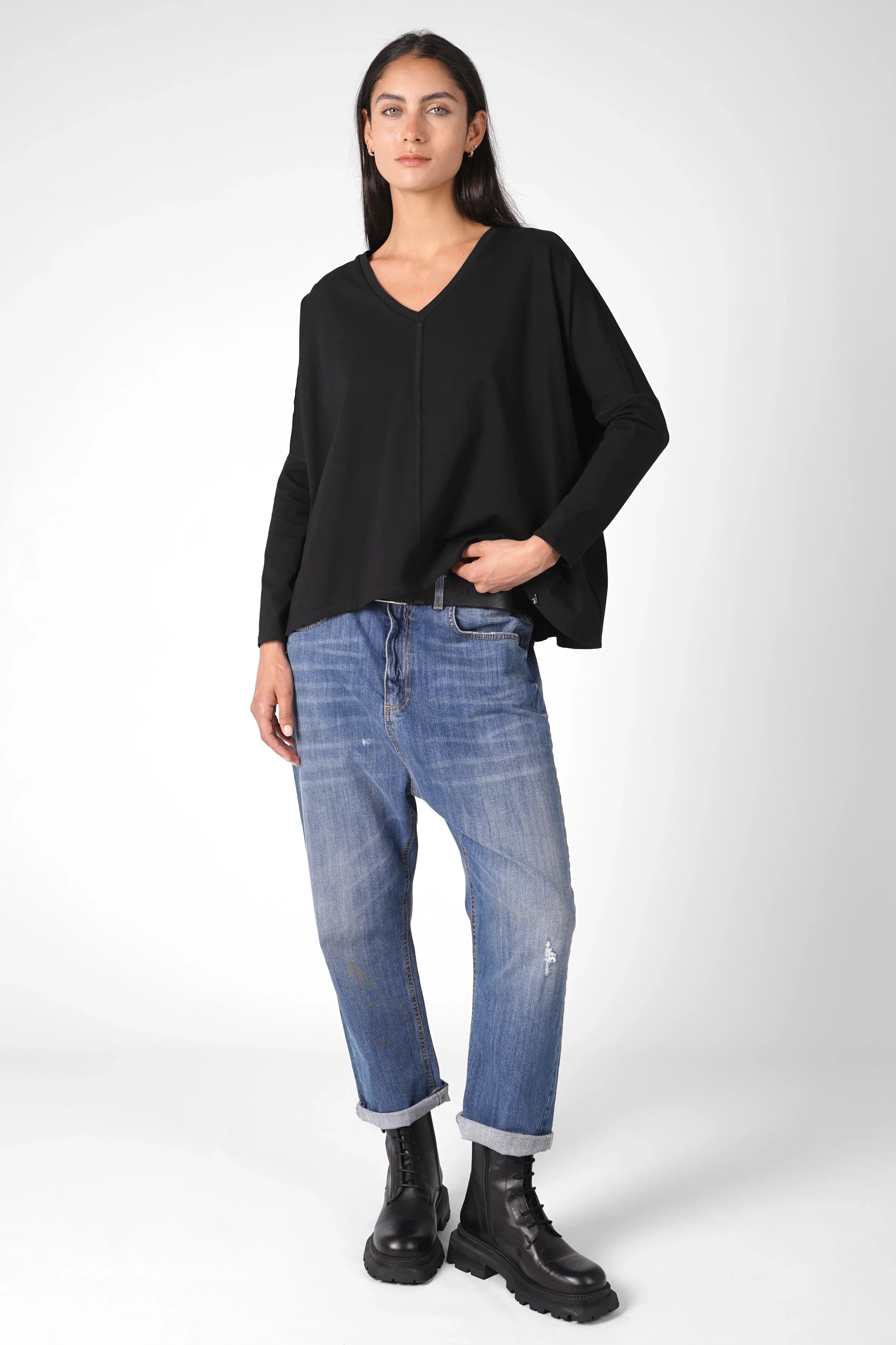 Woman wearing a black TIDA Blusenshirt long-sleeve relaxed fit blouse with V-neck and boxy shape paired with rolled-up blue jeans and black boots.