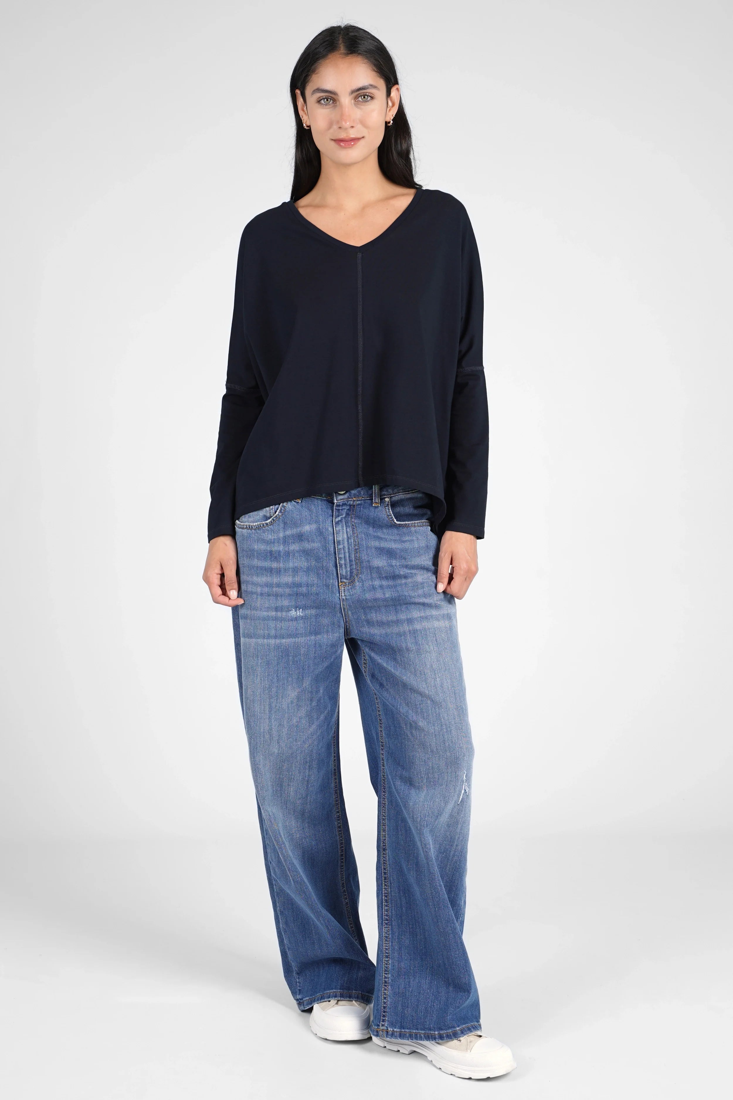 Woman wearing relaxed fit navy TIDA Blusenshirt with V-neck and long sleeves paired with wide-leg jeans and white sneakers