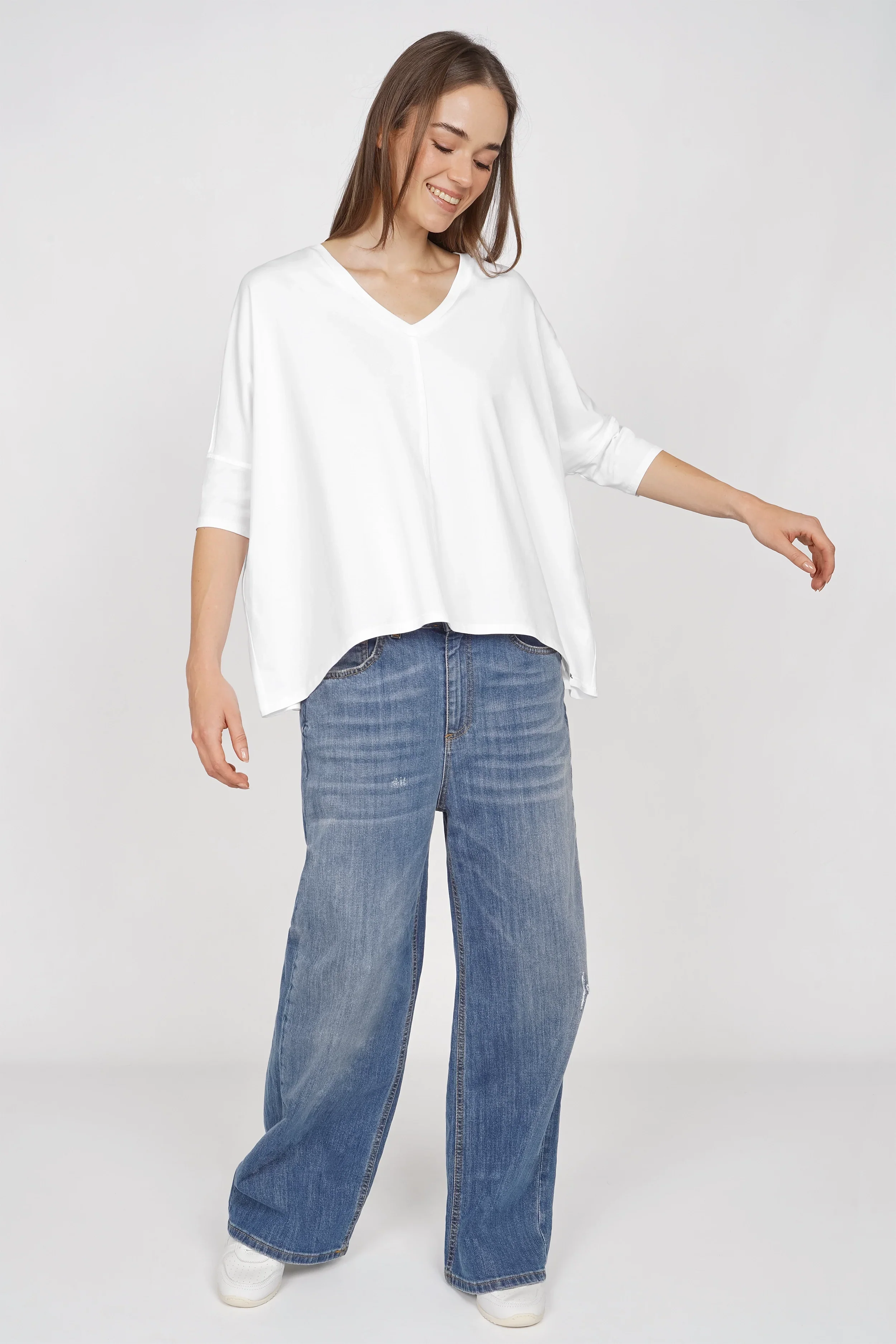 Frau trägt weißes locker fallendes Blusenshirt mit V-Ausschnitt und weiter Kastenform kombiniert mit blauen Jeans