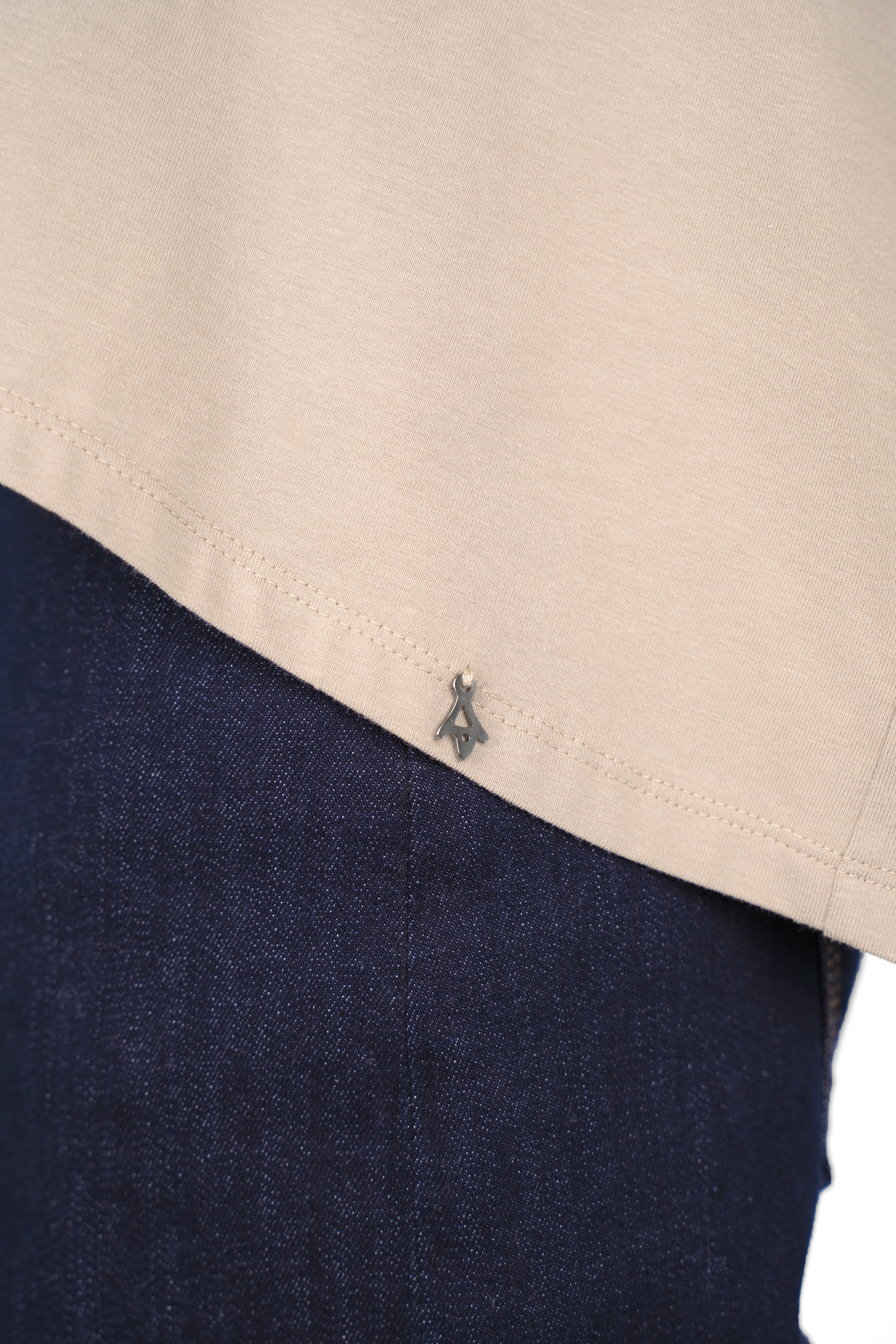 Close-up of beige TIDA Blusenshirt Langarm hem with metal logo detail over dark blue jeans