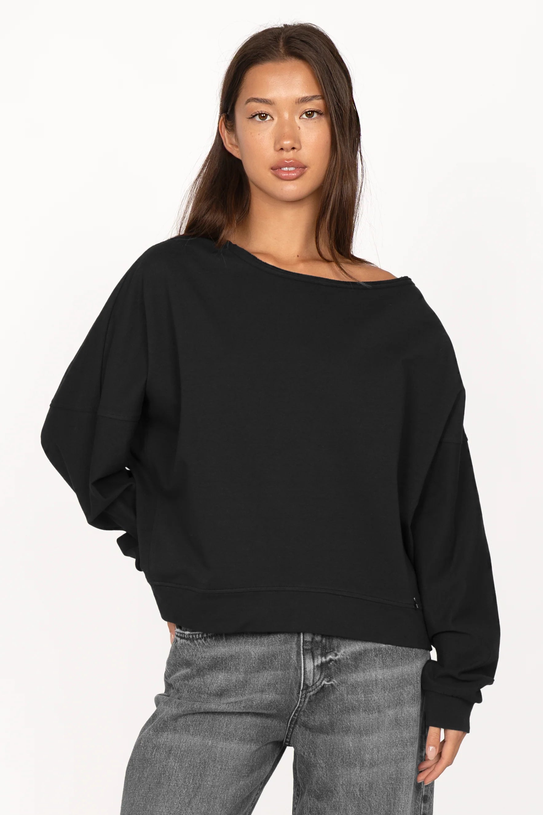 Black one shoulder sweater with wide neckline, relaxed fit, and extended sleeves with cuffs worn by model
