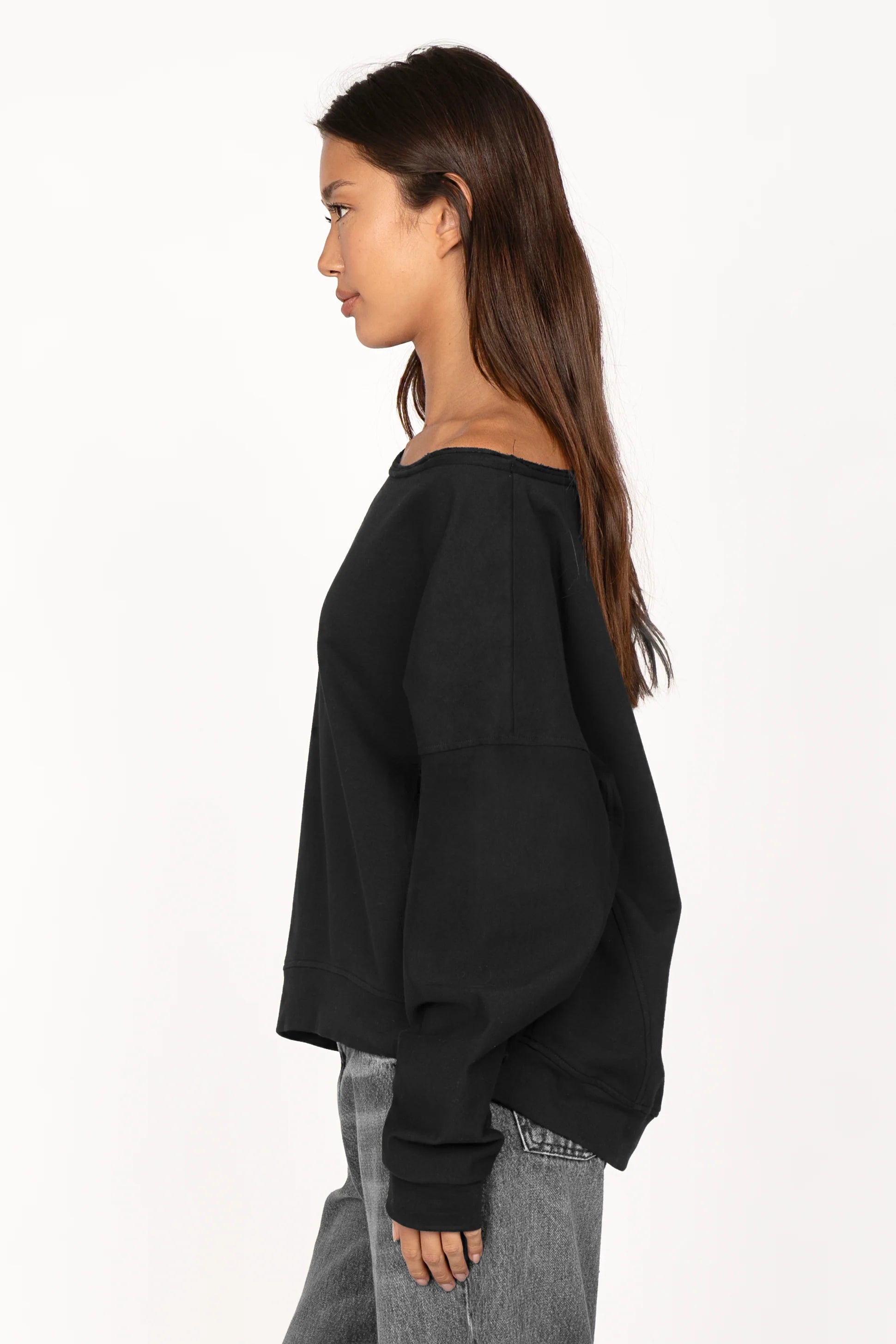 Woman wearing black loose fit one shoulder sweater with wide neckline and extended sleeves against white background