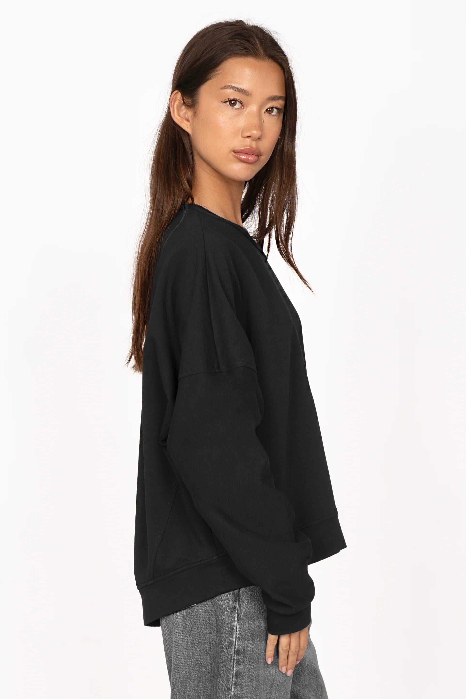 Black one shoulder sweater with loose fit and extended sleeves worn by female model in side view