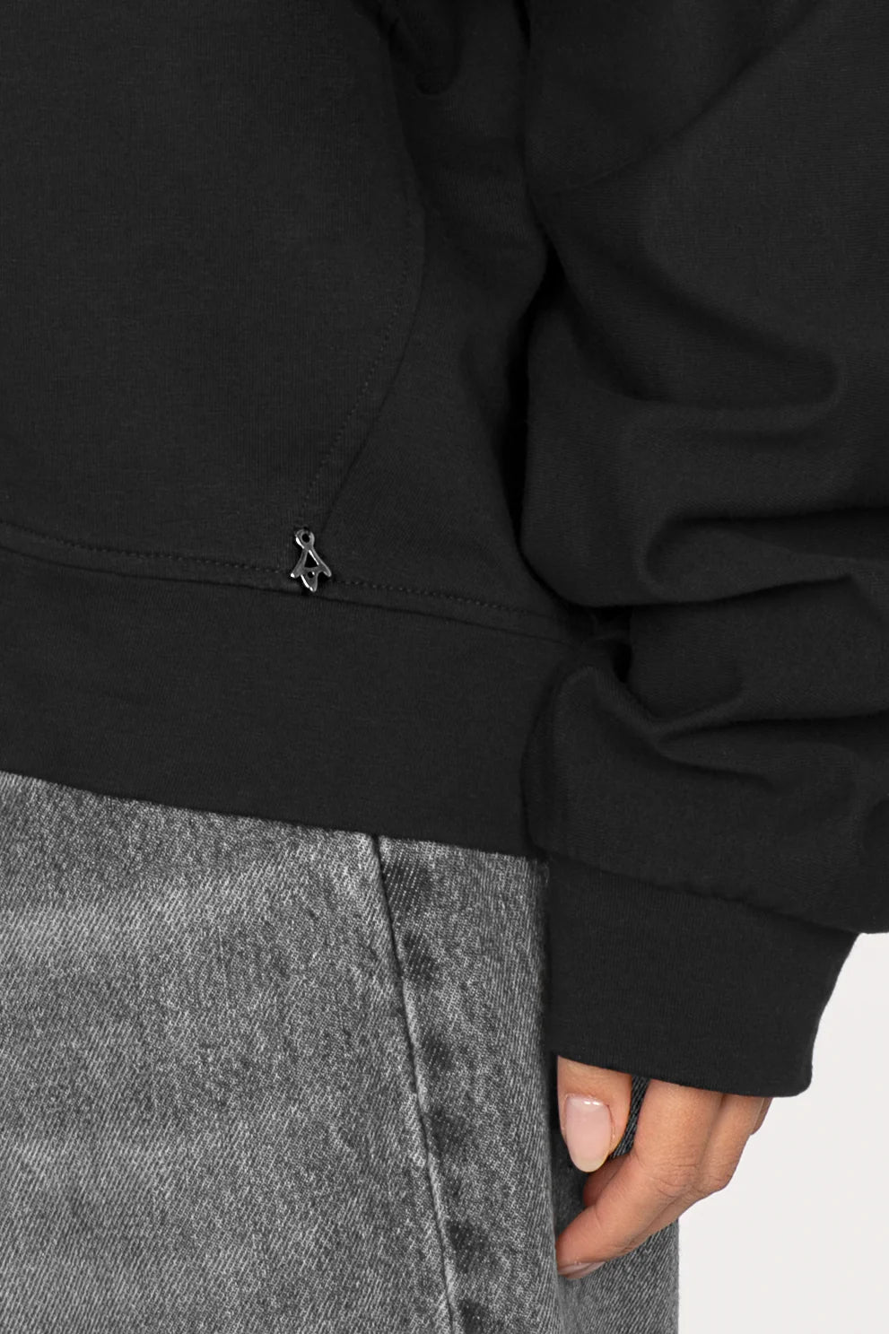 Black one shoulder sweater with cuffed sleeves and relaxed fit worn with gray jeans