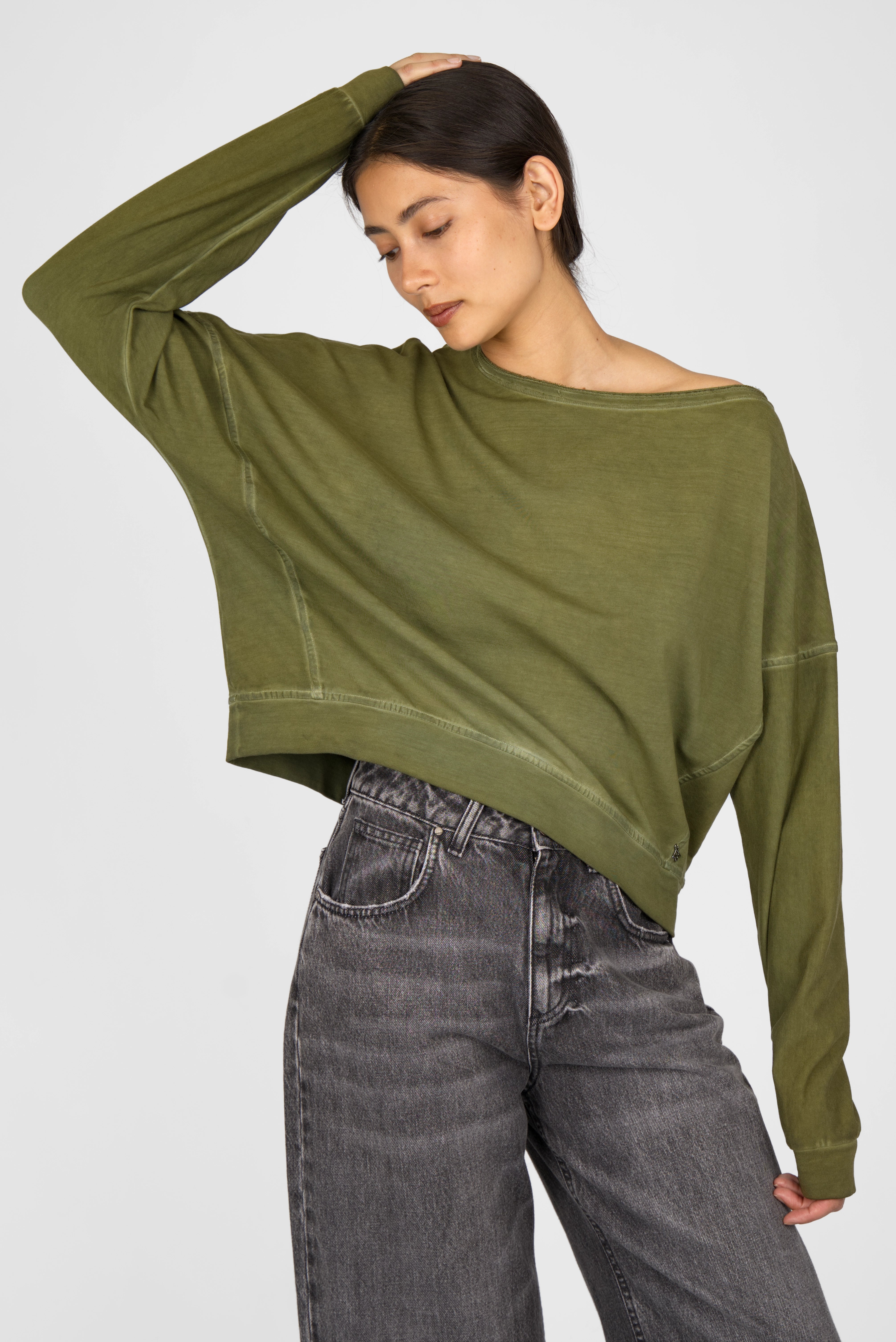 TIMAJ Revive One Shoulder Sweater in olive green with loose fit and wide neckline featuring open edges, worn with gray jeans