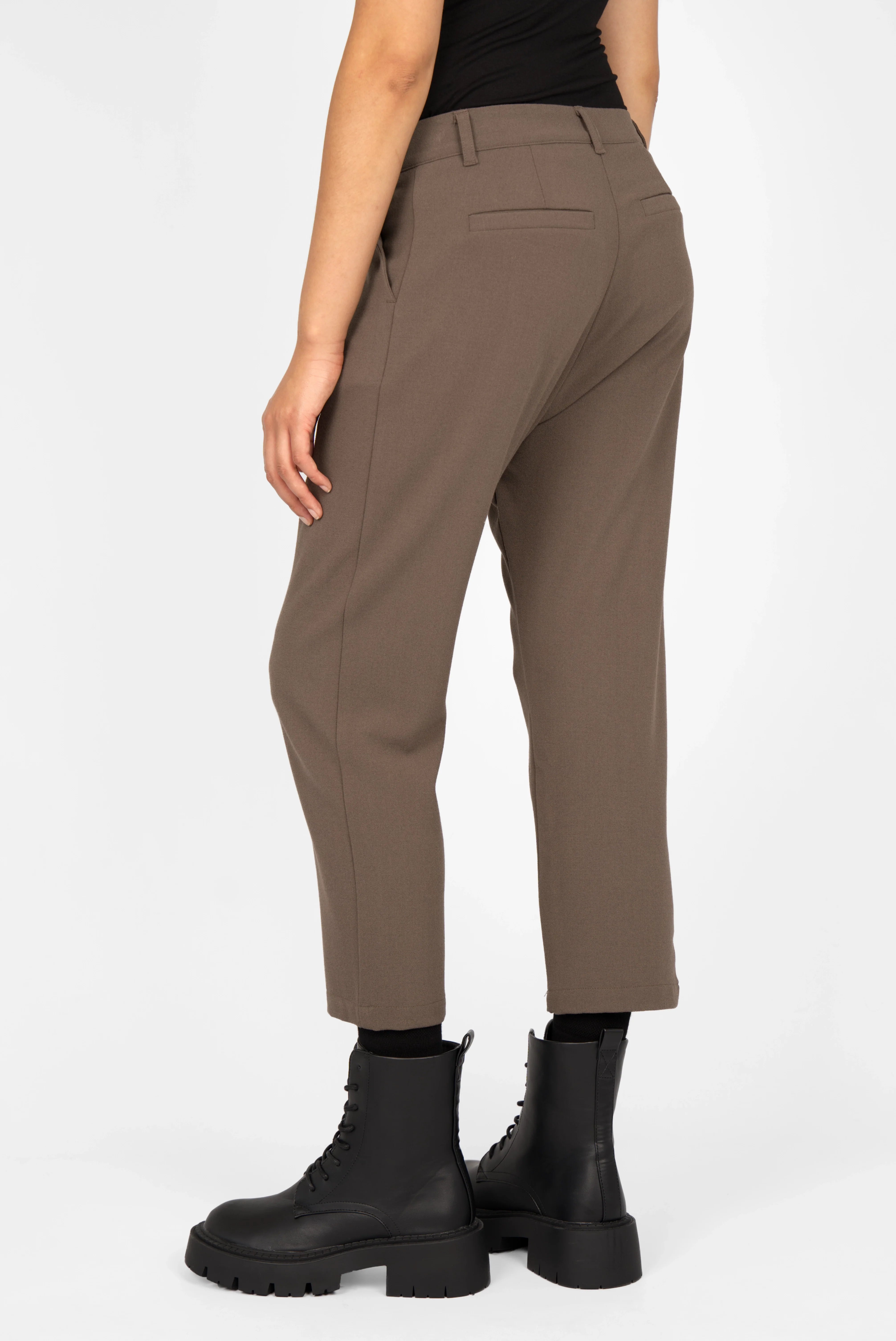 Back view of TINKE cropped fit pants in brown with a relaxed hip fit and subtle pleats, worn with black ankle boots.