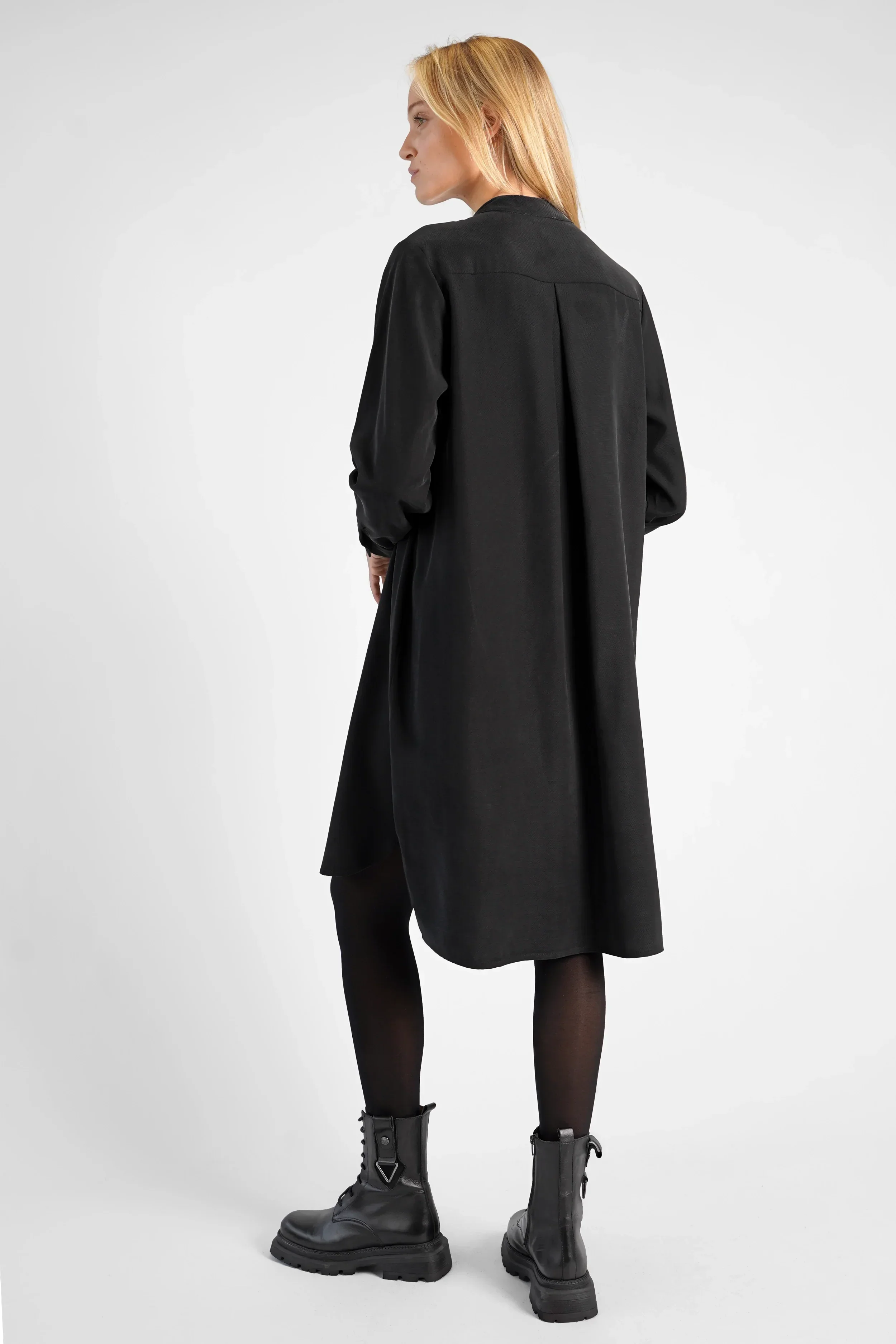 Black lyocell-blend blouse dress with stand-up collar, button front, long sleeves, and longer back hem worn by model.