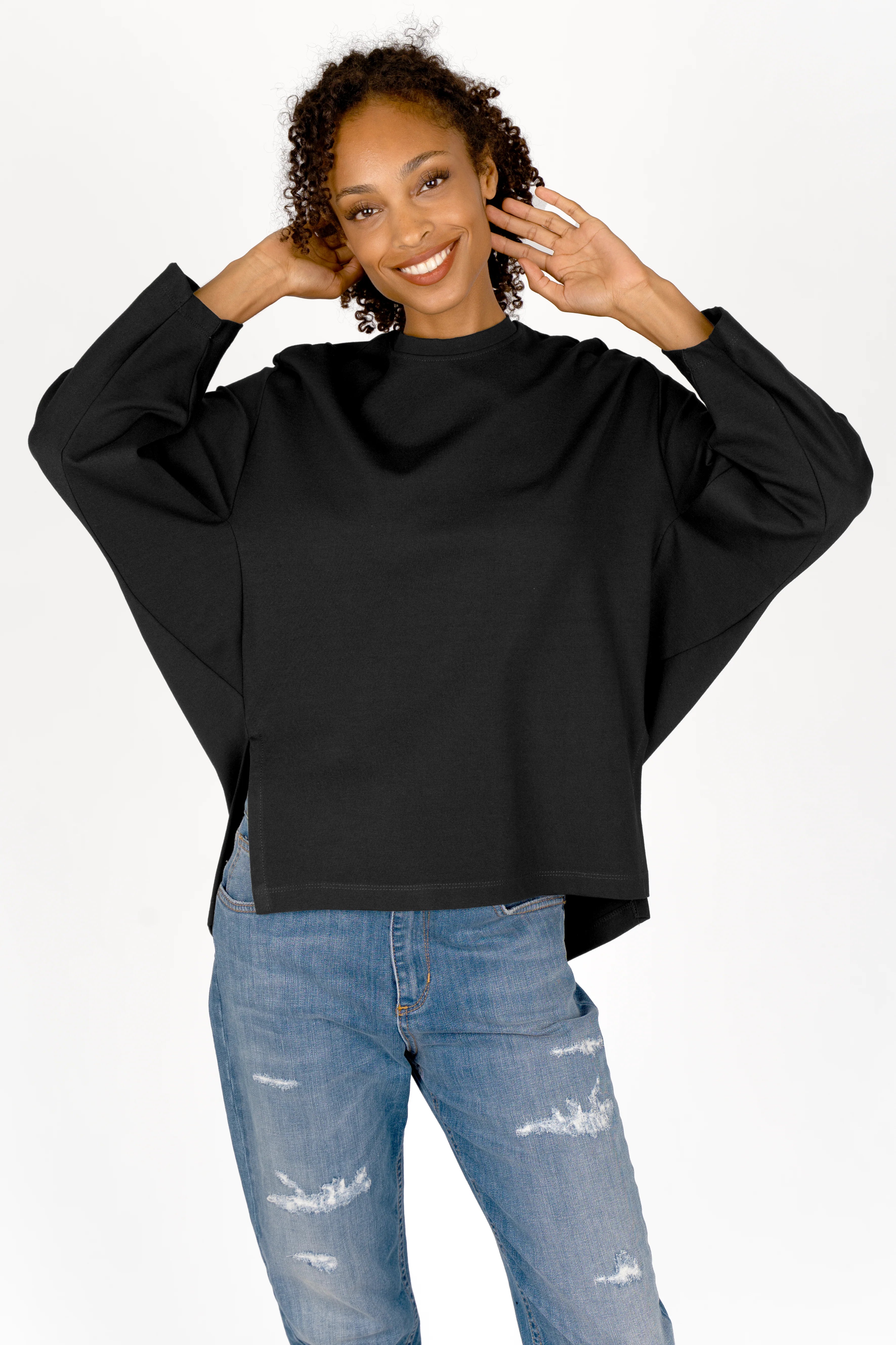 Woman wearing a black TOOVE Shirt in relaxed fit with rounded neckline, extended back, high side slits, and dropped shoulders paired with ripped blue jeans.