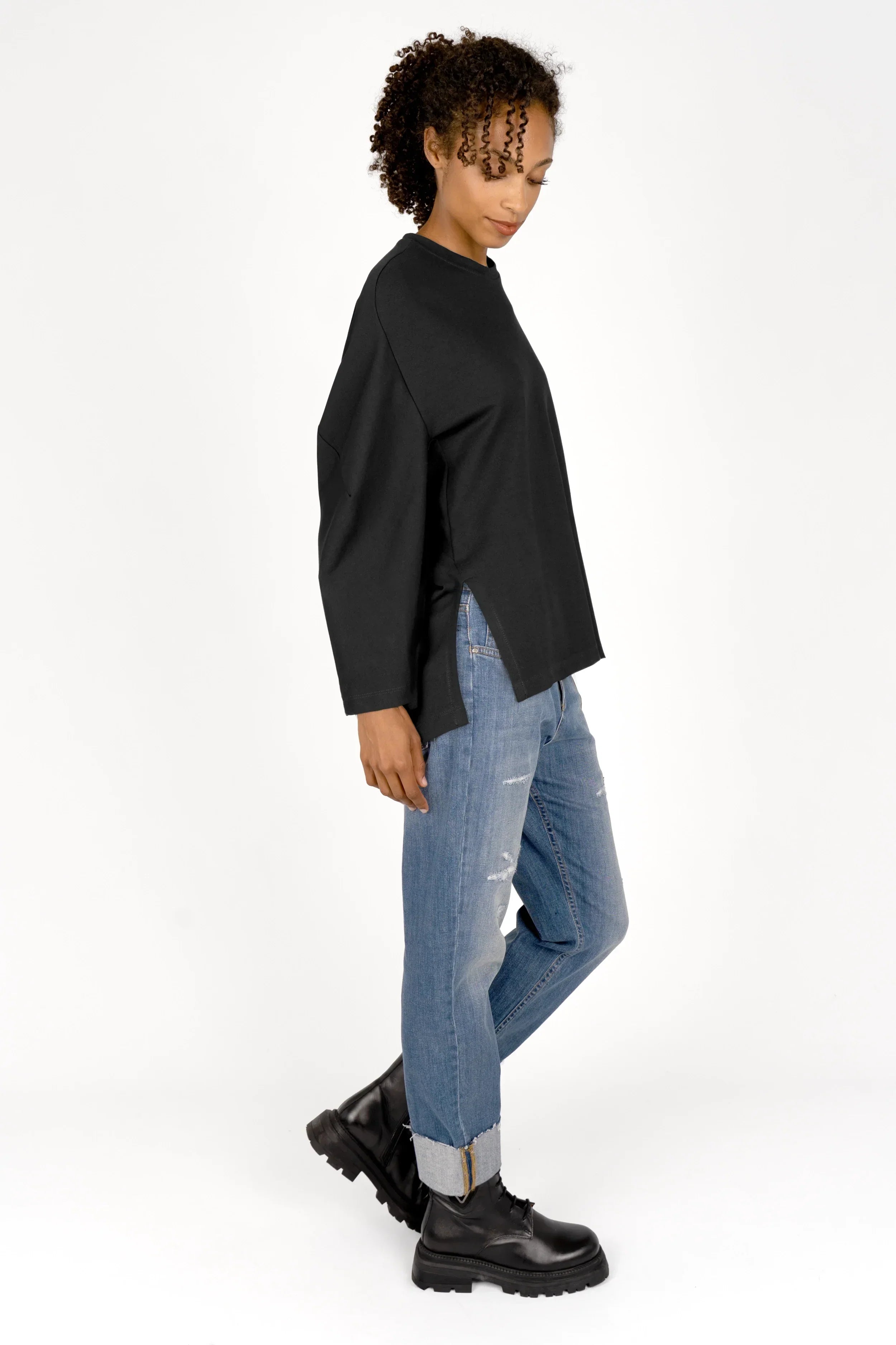 Frau trägt schwarzes TOOVE Shirt aus elastischem Interlock-Jersey mit Rundhalsausschnitt und hohen Seitenschlitzen