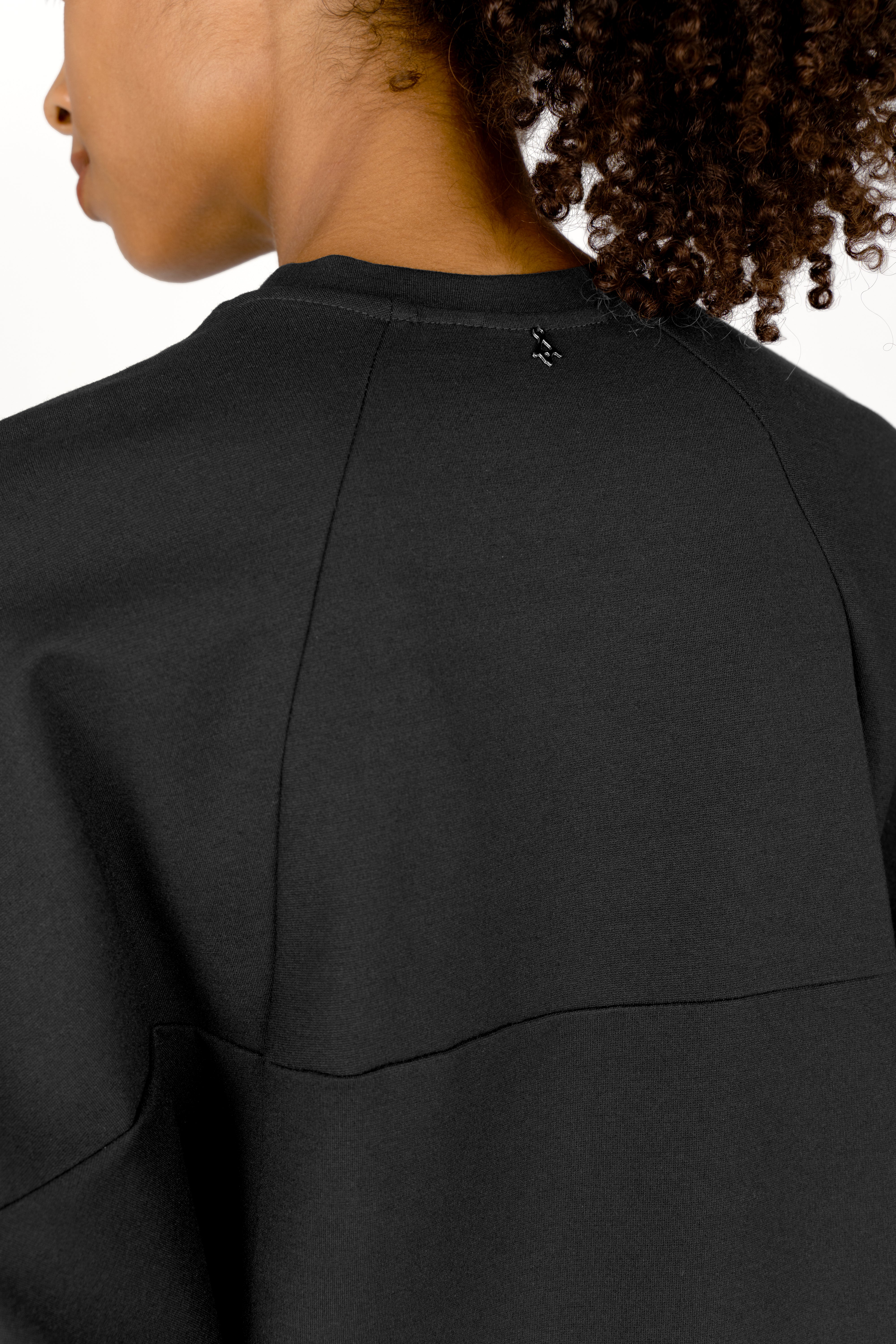 Back view of black TOOVE Shirt with relaxed fit and curved seam details on stretchy interlock jersey fabric
