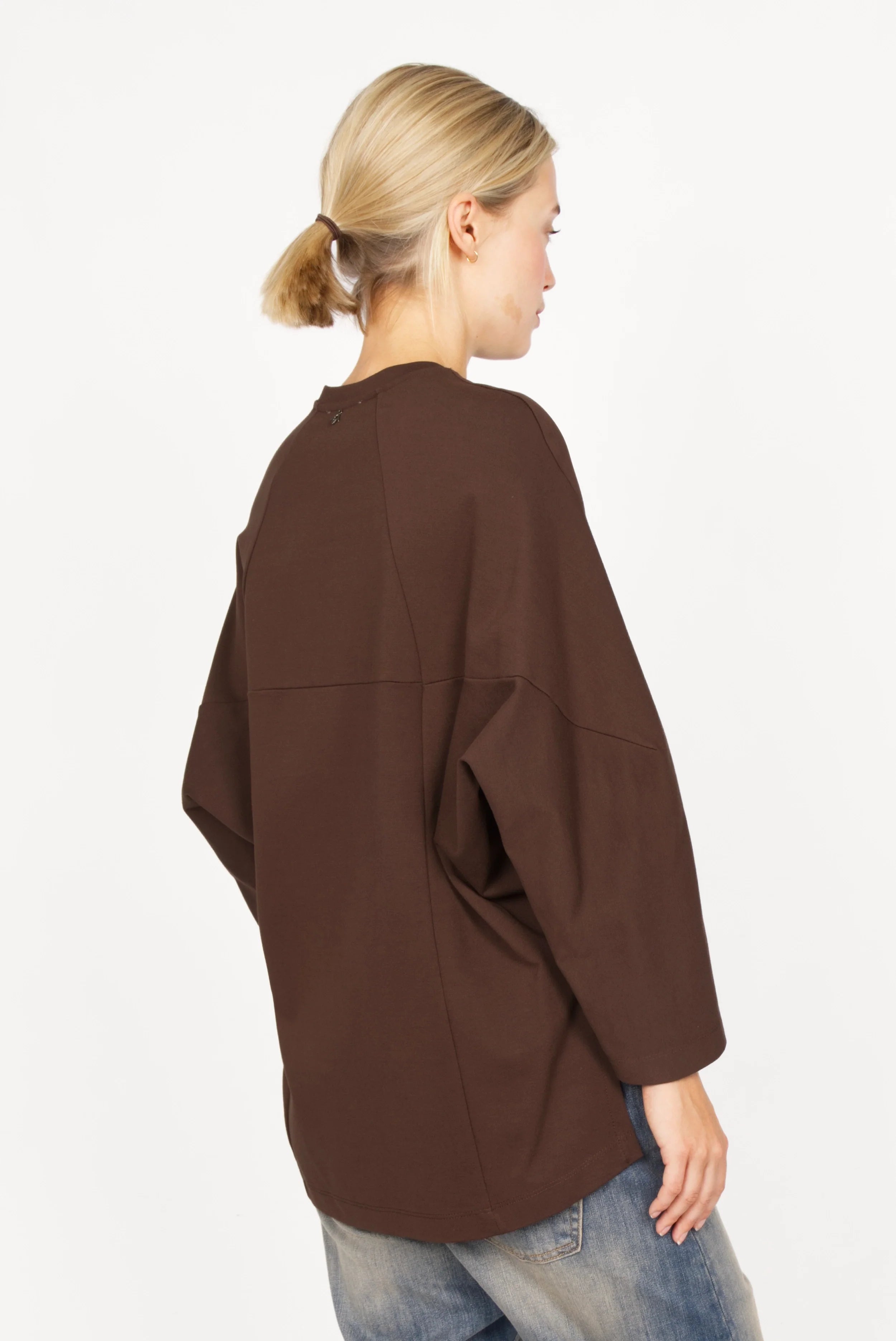 Damen trägt braunes TOOVE Shirt aus mittelschwerem Interlock-Jersey mit verlängertem Rücken und geschwungenen Teilungsnähten, Rückansicht.