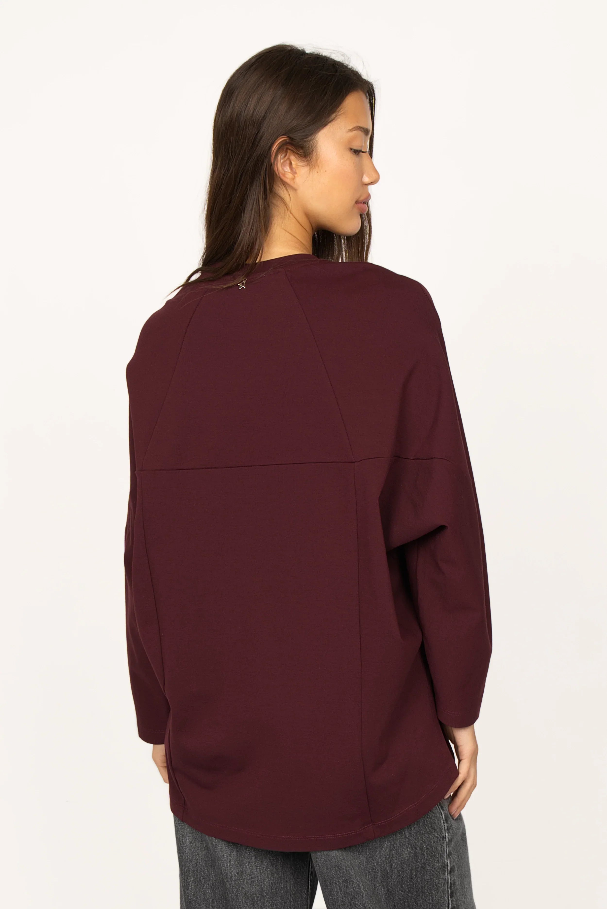 Frau trägt locker geschnittenes TOOVE Shirt in Bordeaux mit geschwungenen Nähten und verlängerter Rückenpartie aus mittelschwerem Interlock-Jersey