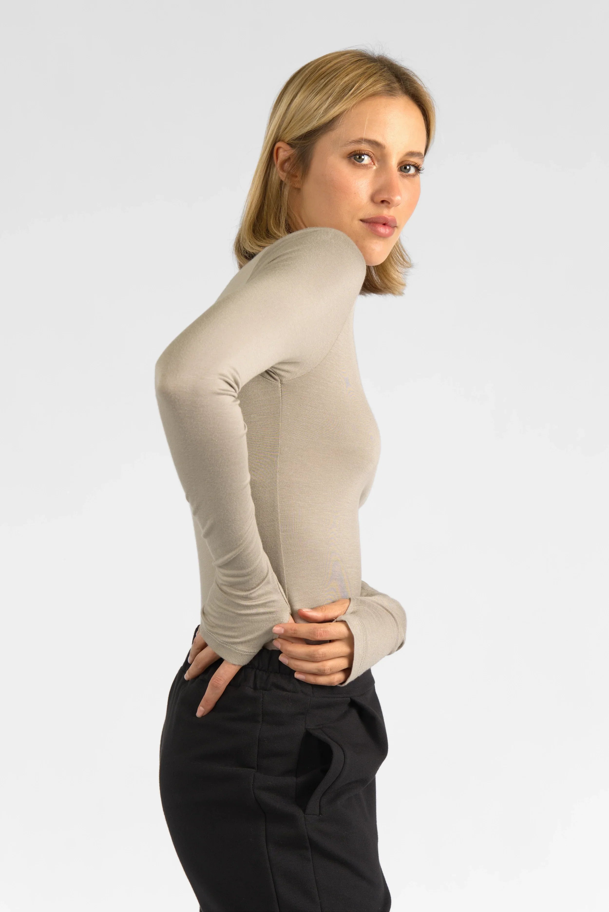 Woman wearing beige VALUM Longsleeve with thumbholes and black pants, side view