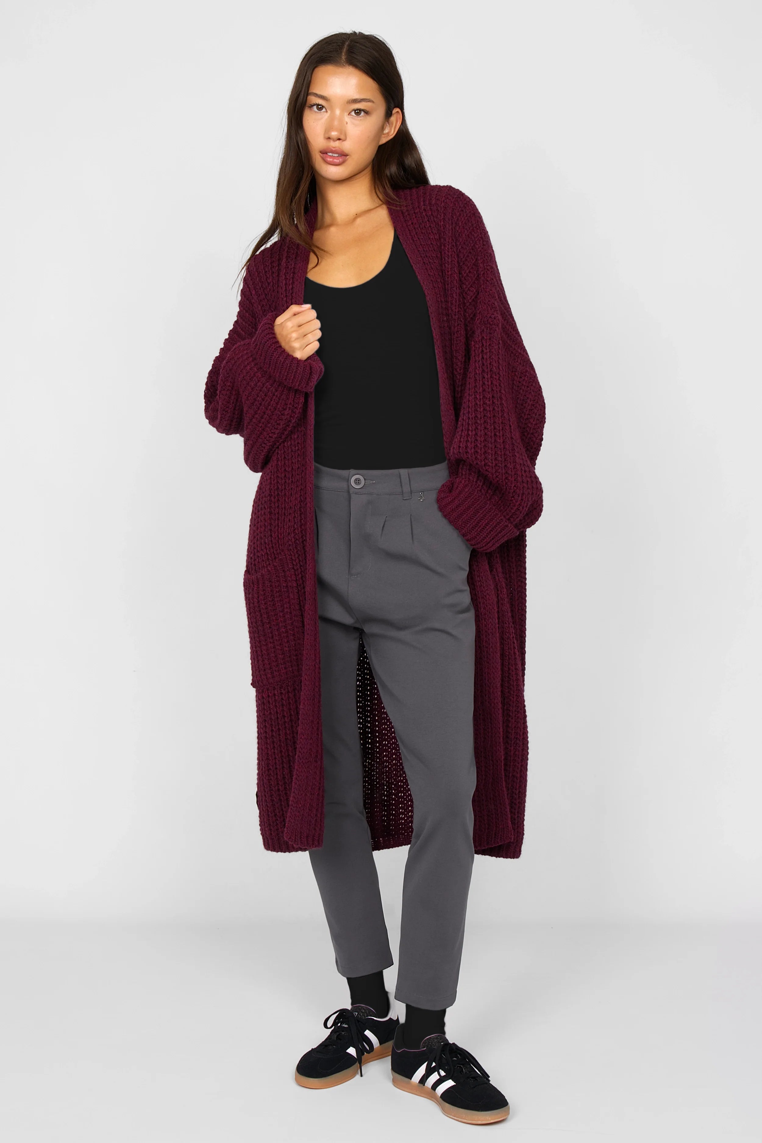 Frau trägt HEELENA Tapered Pants in Grau mit bordeauxrotem Strickmantel und schwarzem Top