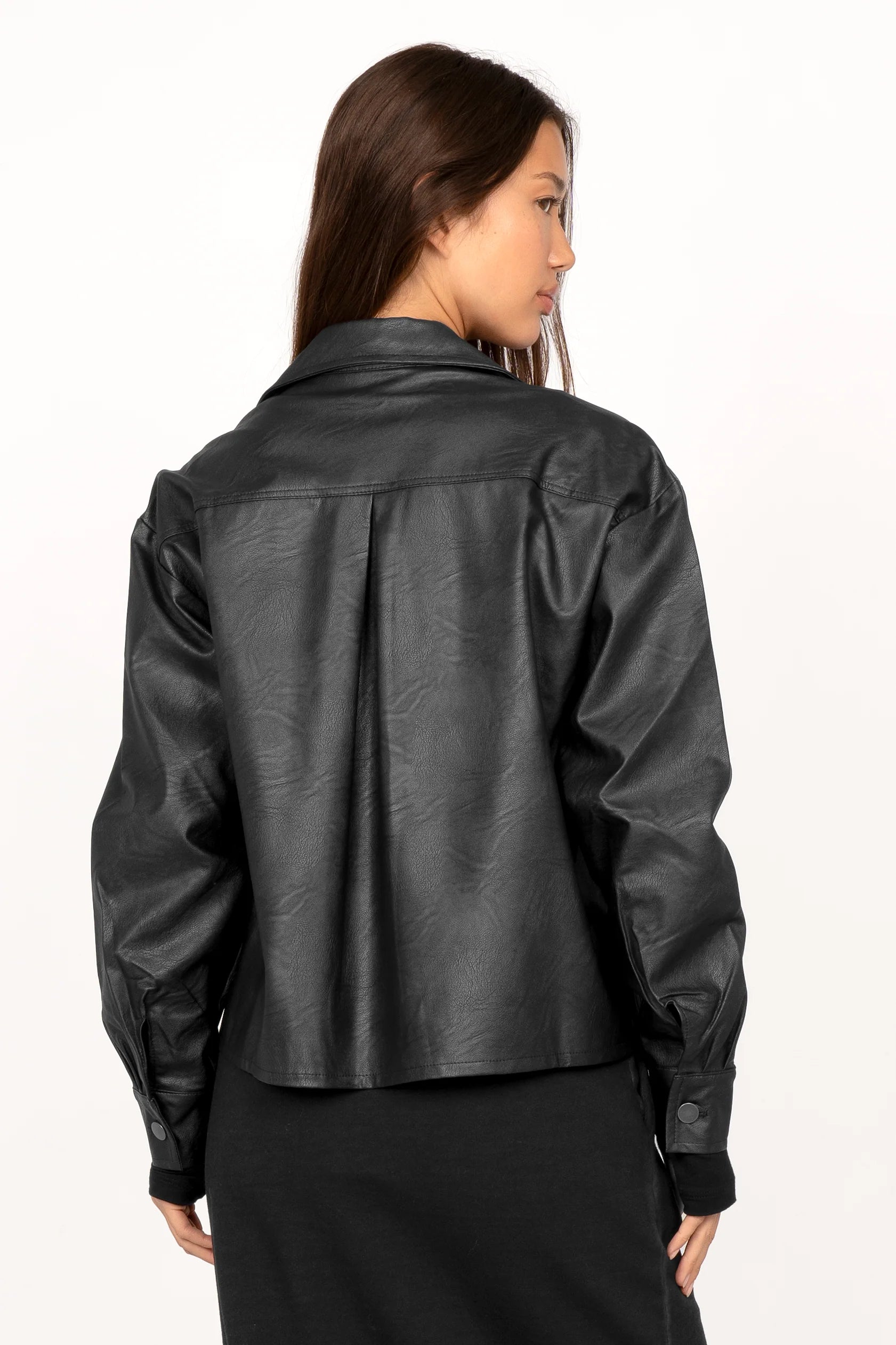 Back view of a woman wearing a cropped black eco-leather Hemdjacke with Kent collar and slightly dropped shoulders.