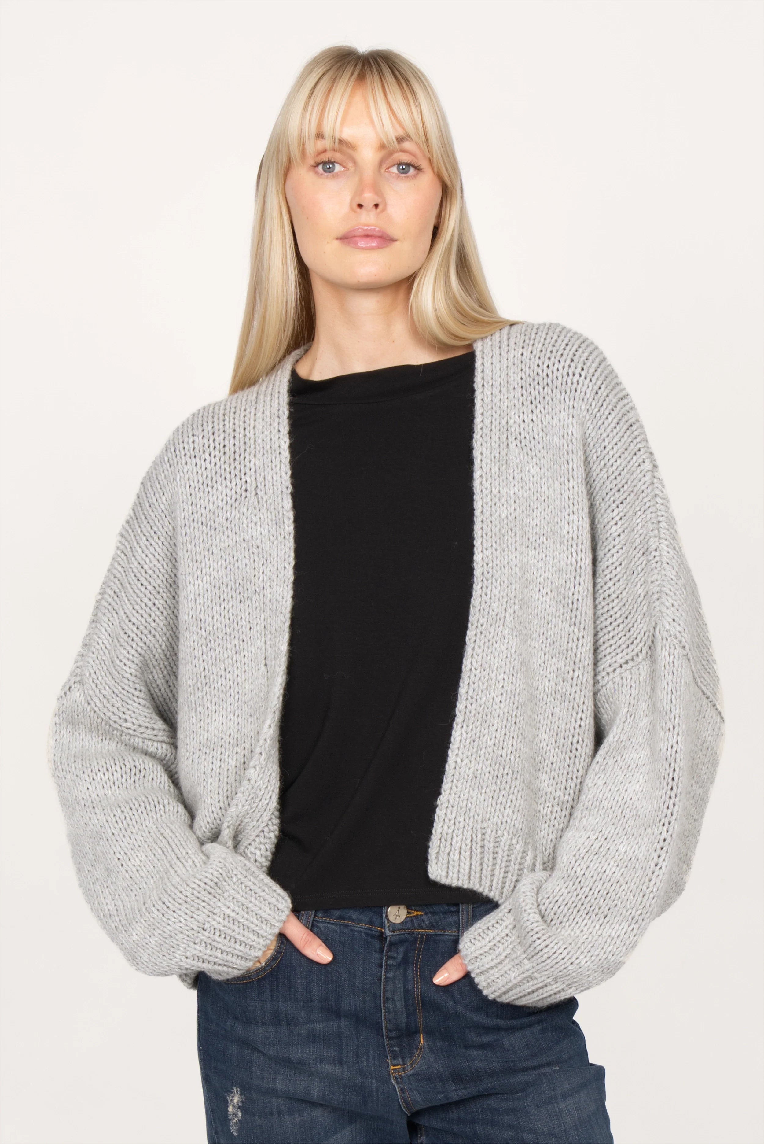 Woman wearing ALIXA Cropped Strickcardigan in grey with loose fit and ribbed cuffs over black top and jeans