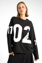 Black AGA Statement Sweater with bold white number prints on chest and sleeves, round neckline, regular fit, worn by female model