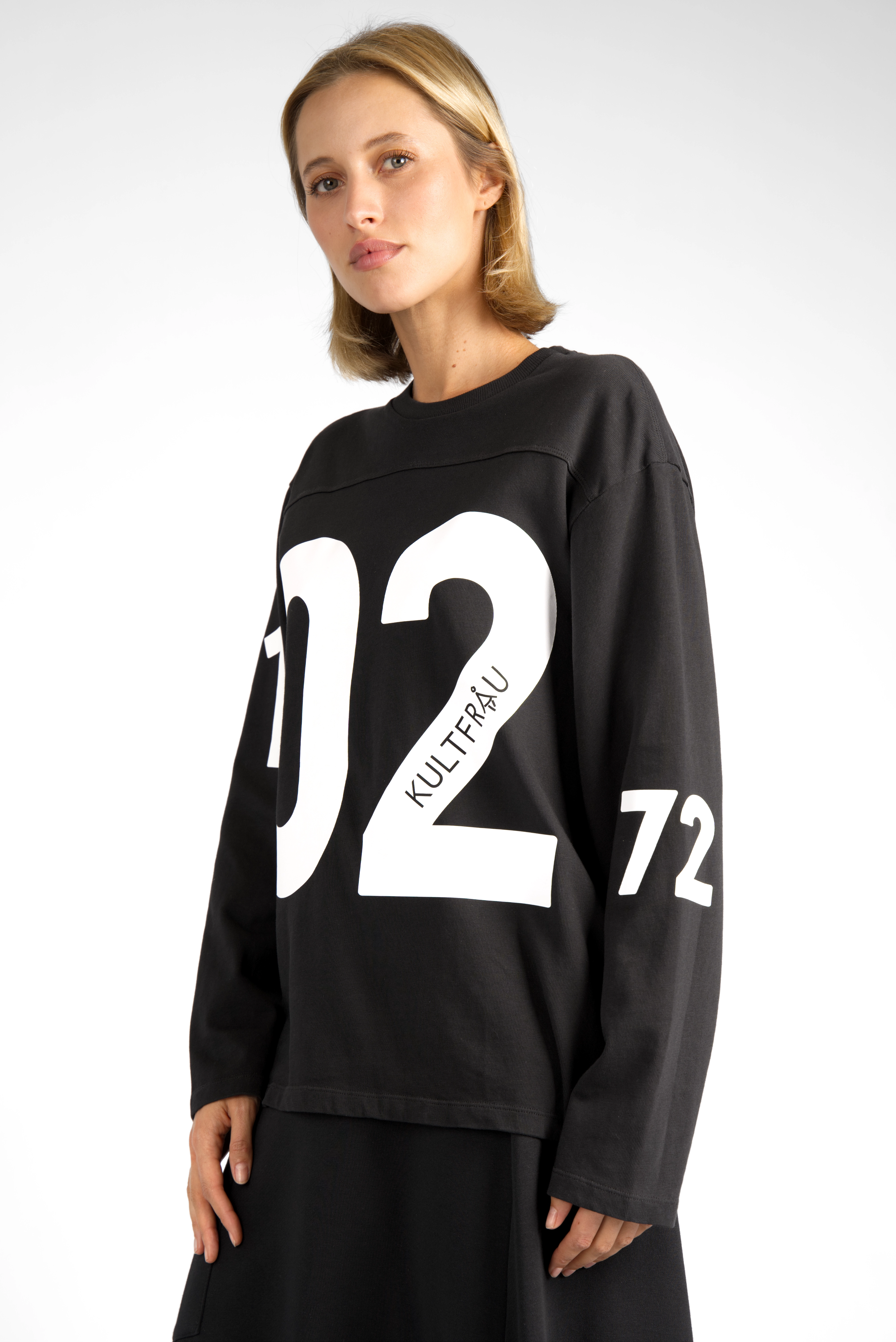 Woman wearing black AGA Statement Sweater with bold white number print on chest and sleeves in regular fit.