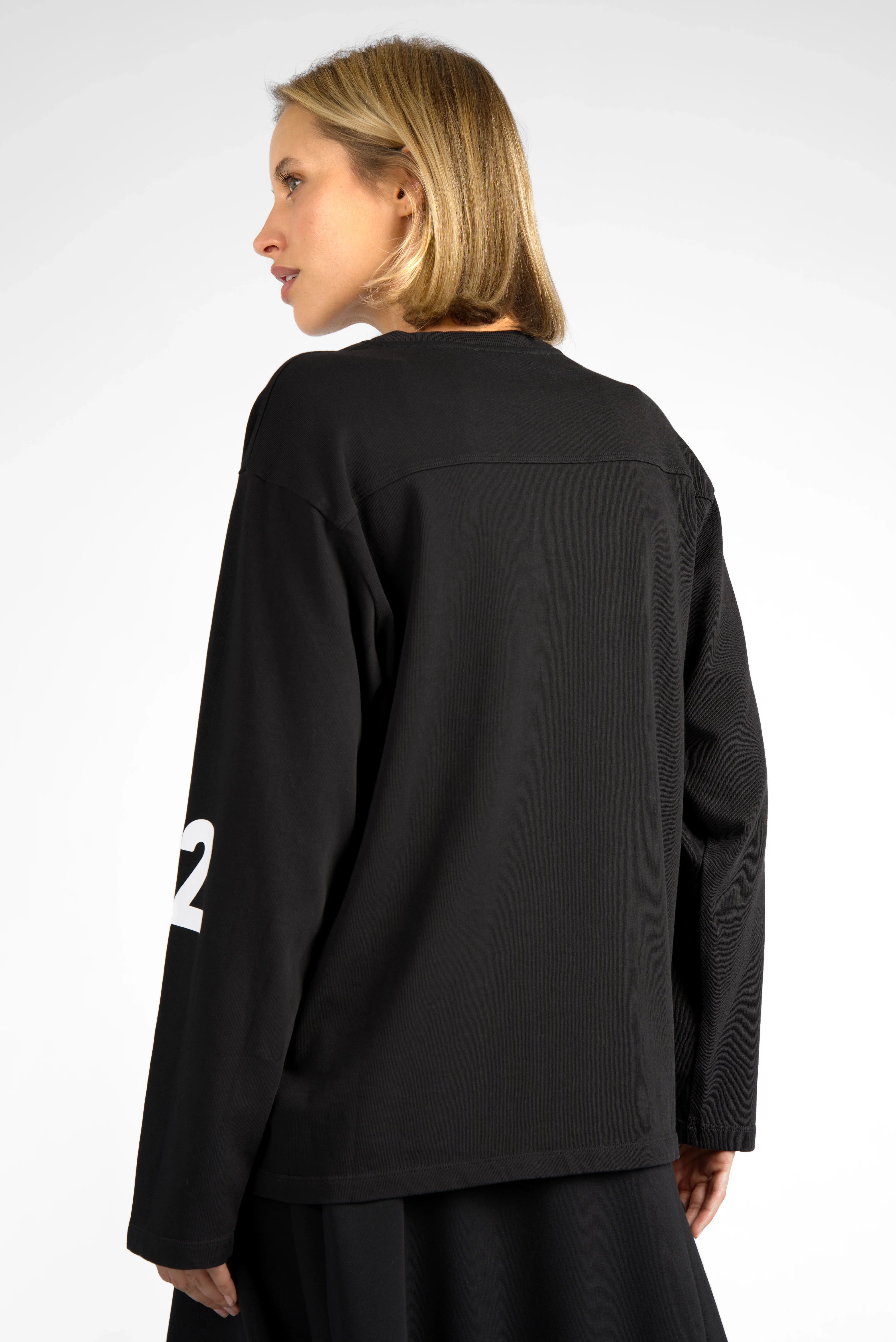 Back view of AGA Statement Sweater in black cotton jersey with white number print on sleeves, worn by model