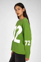 Green AGA Statement Sweater with bold white number print on front and sleeves, worn by female model.