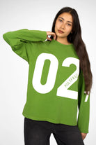 Green oversized AGA Statement Sweater with white bold number print on front and sleeves, worn by a model with long dark hair.
