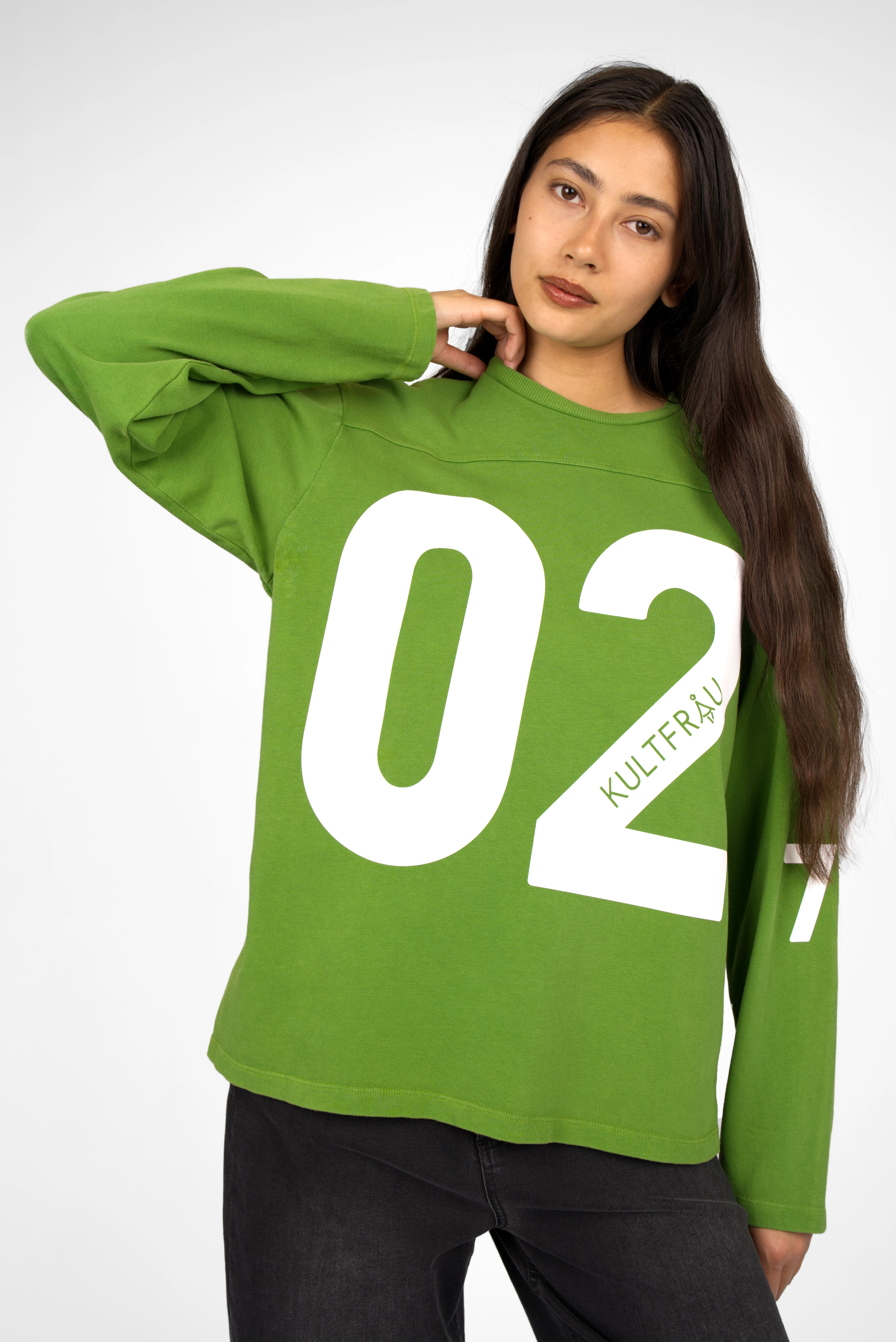 Green oversized AGA Statement Sweater with white bold number print on front and sleeves, worn by a model with long dark hair.