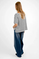 Back view of woman wearing AILIE T-Shirt with black and white stripes and regular fit paired with blue wide-leg jeans