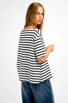 Woman wearing AILIE T-Shirt in black and white stripes with a minimalist boat neckline and dropped shoulders.