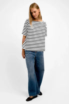 Woman wearing AILIE T-Shirt with black and white stripes and blue jeans standing against white background