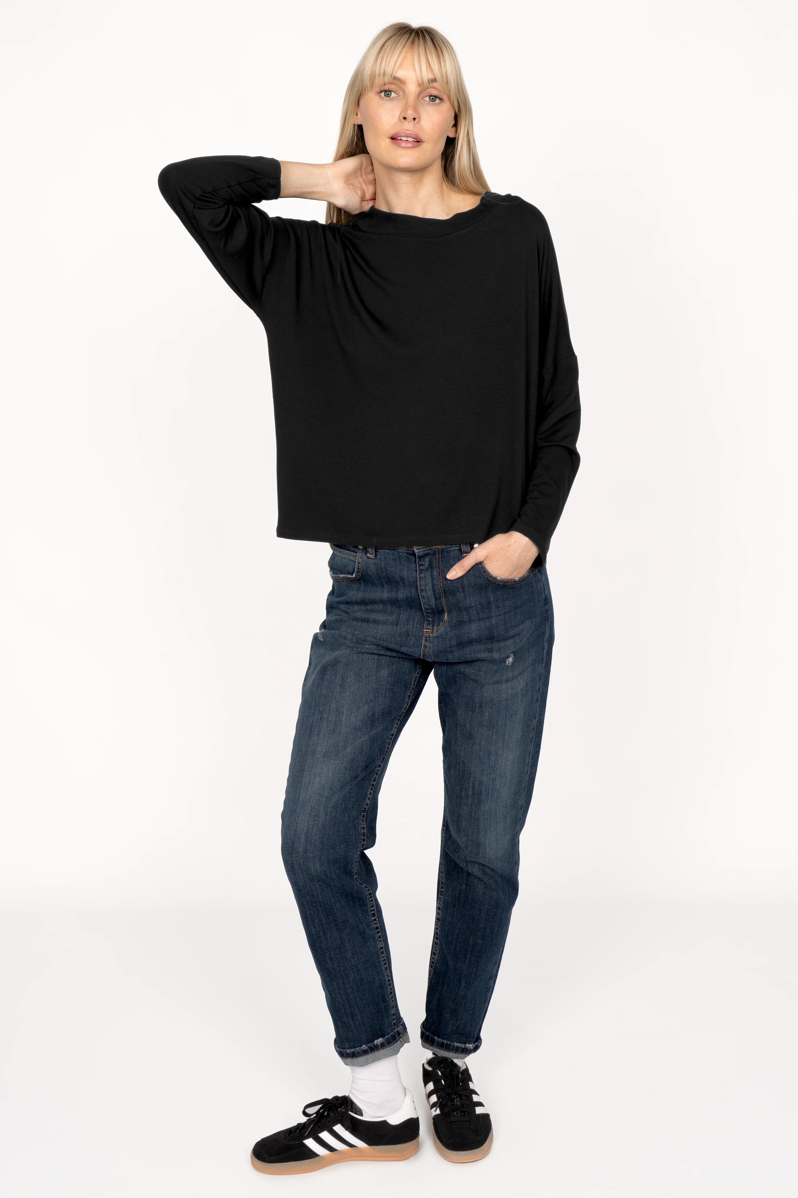 Woman wearing black ALFERA longsleeve made of lightweight viscose jersey with loose neckline and long sleeves, paired with blue jeans and black sneakers.