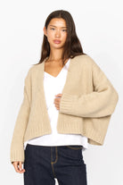 Woman wearing beige ALIXA Cropped Strickcardigan with loose fit, ribbed cuffs, and shawl collar over white top and jeans