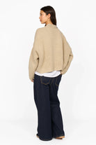 Woman wearing beige ALIXA Cropped Strickcardigan with loose fit and dropped shoulders, paired with dark wide-leg jeans, shown from back.